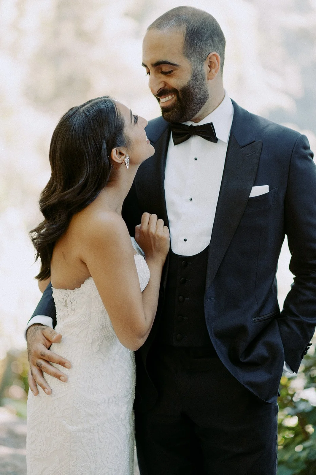 A man and woman in wedding attire sharing a moment, smiling at each other.
