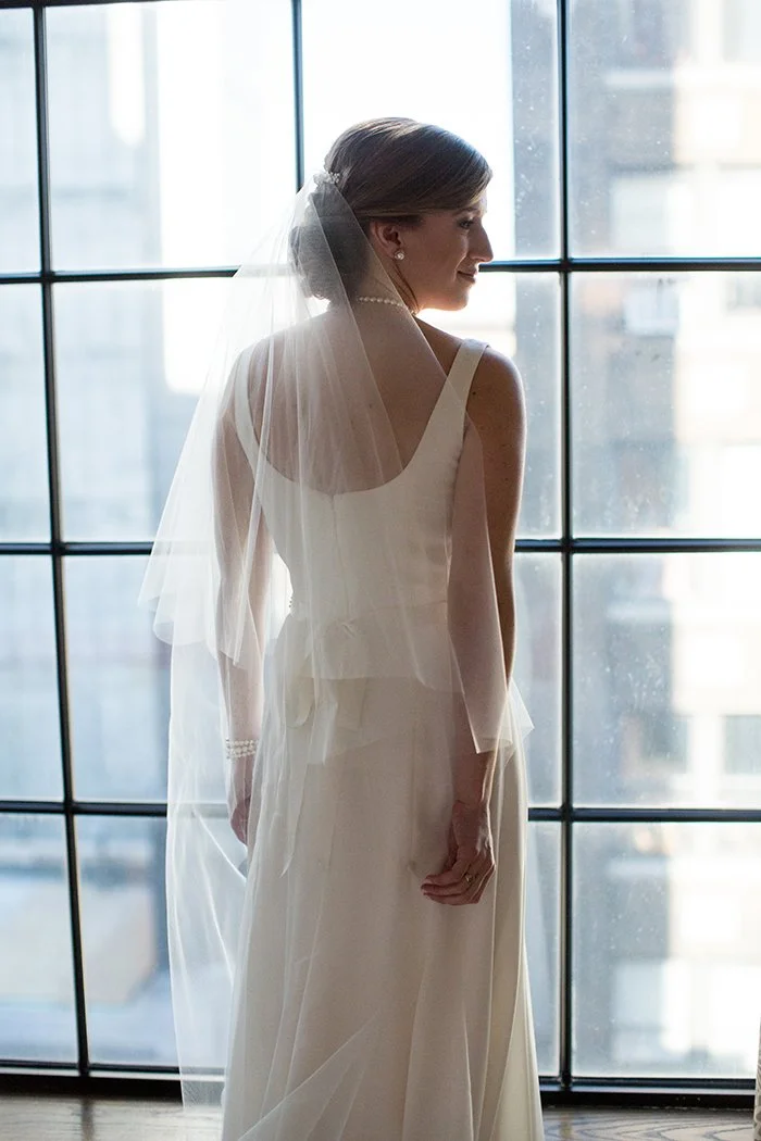 Bride in a white wedding dress and veil standing in front of a large window.