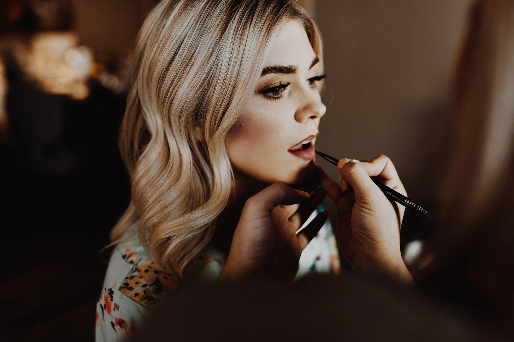 A woman with blonde hair getting her makeup done by a makeup artist.