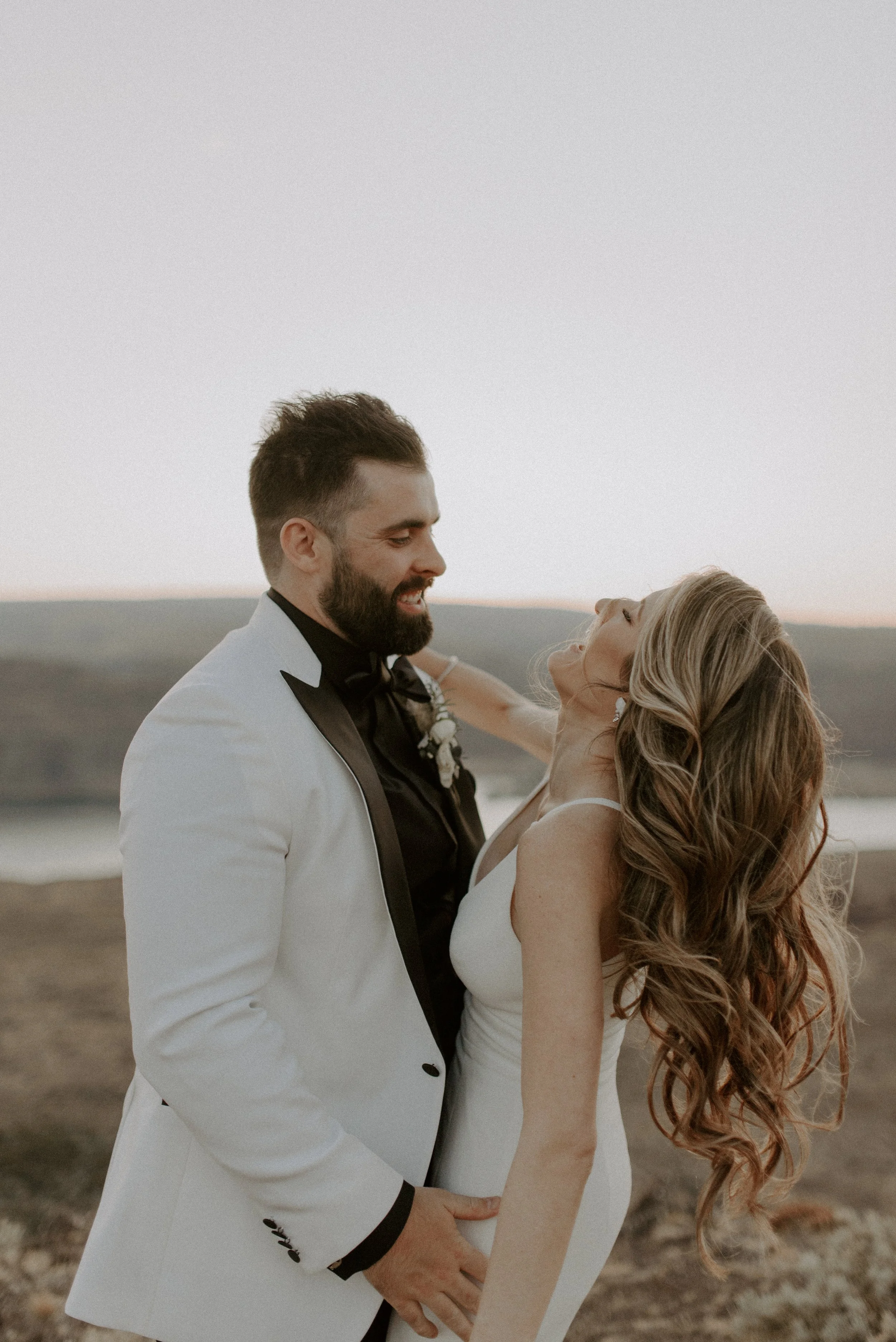 A newlywed couple dancing outdoors during sunset, with a scenic landscape in the background.