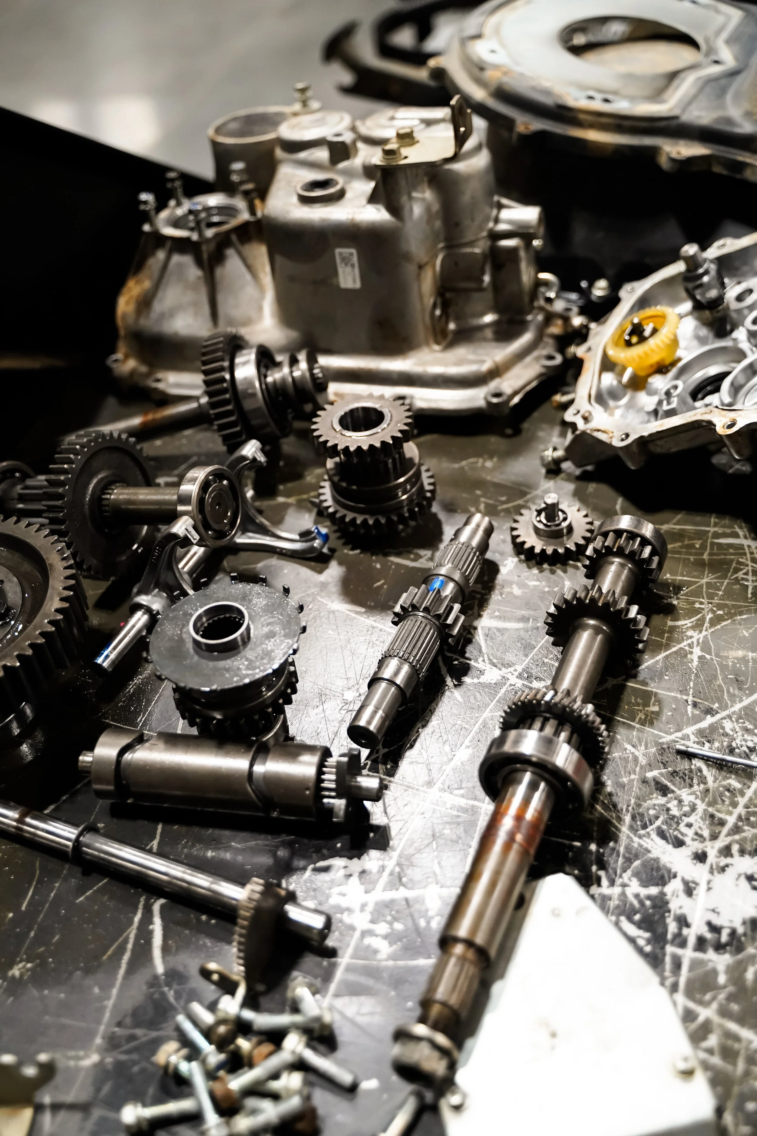Disassembled engine parts, gears, shafts, and screws on a worktable, with an engine casing in the background.