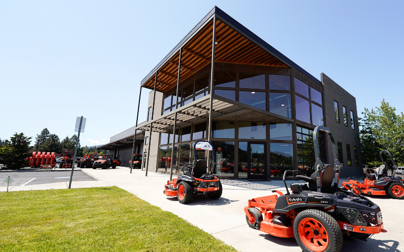 Modern commercial building with extensive glass windows, surrounded by outdoor machinery and equipment, on a sunny day.