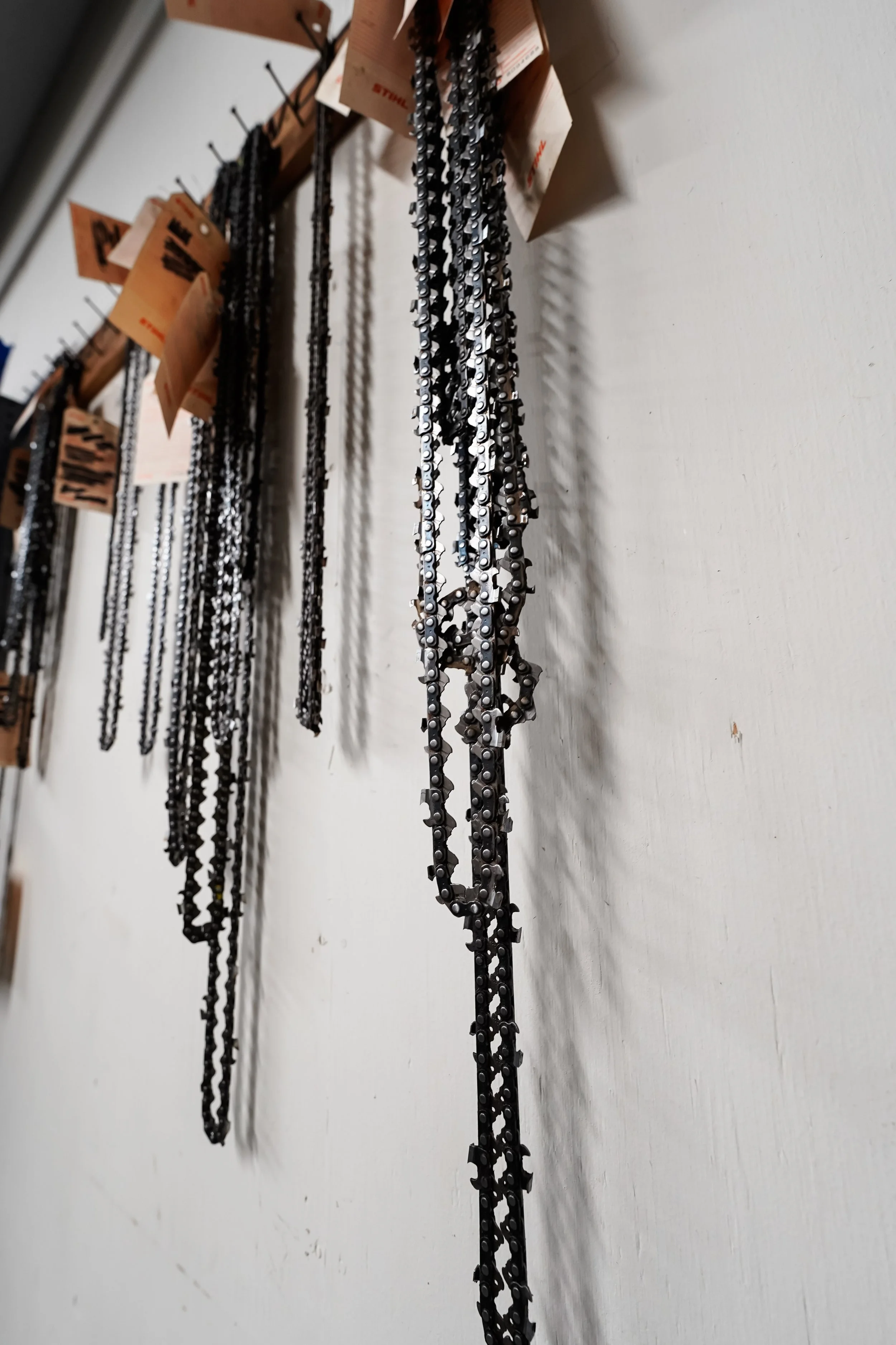 String of chains hanging on hooks, with tags attached, on a wall.