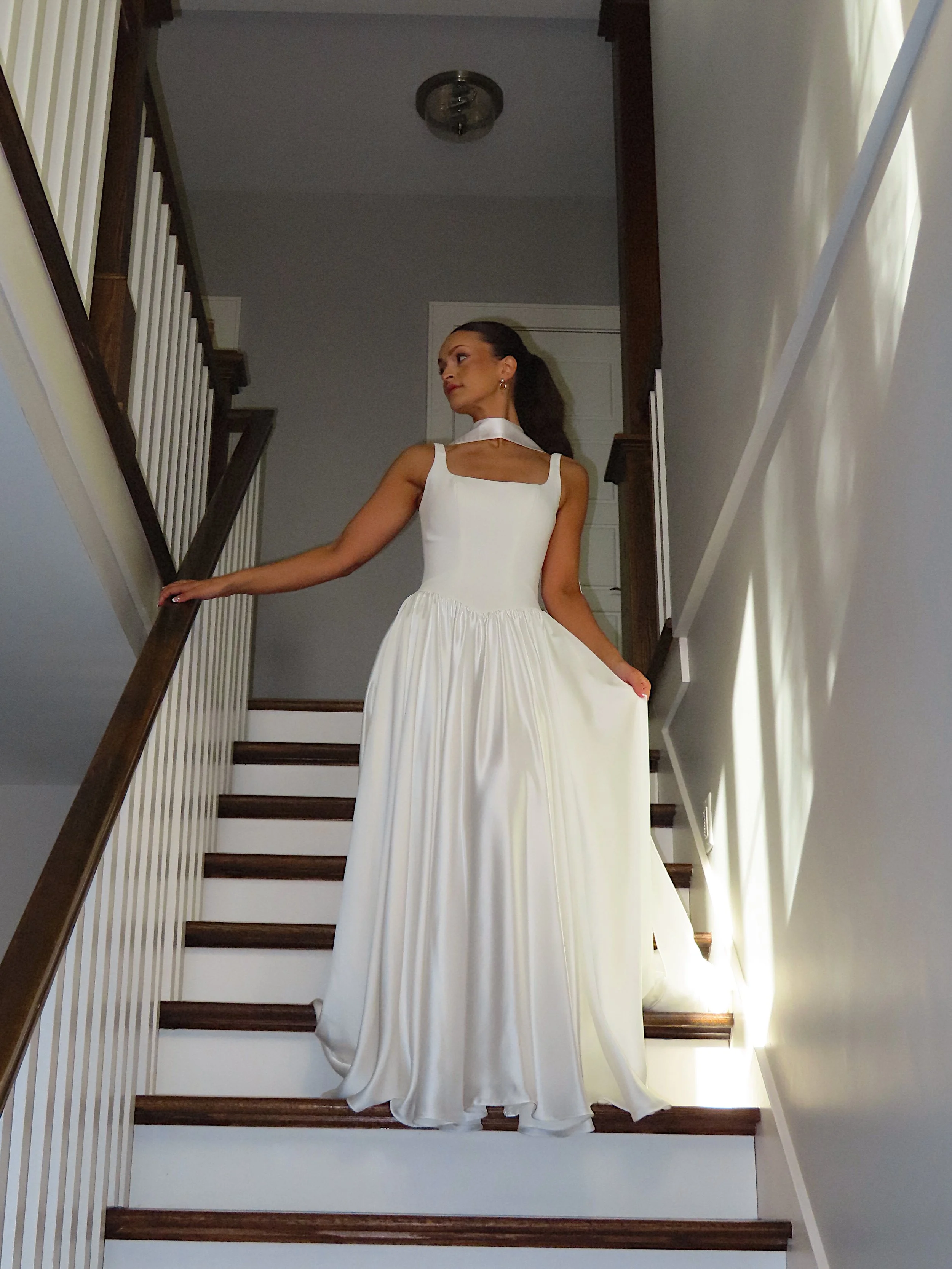 A woman in a white dress standing on a staircase in a modern home.