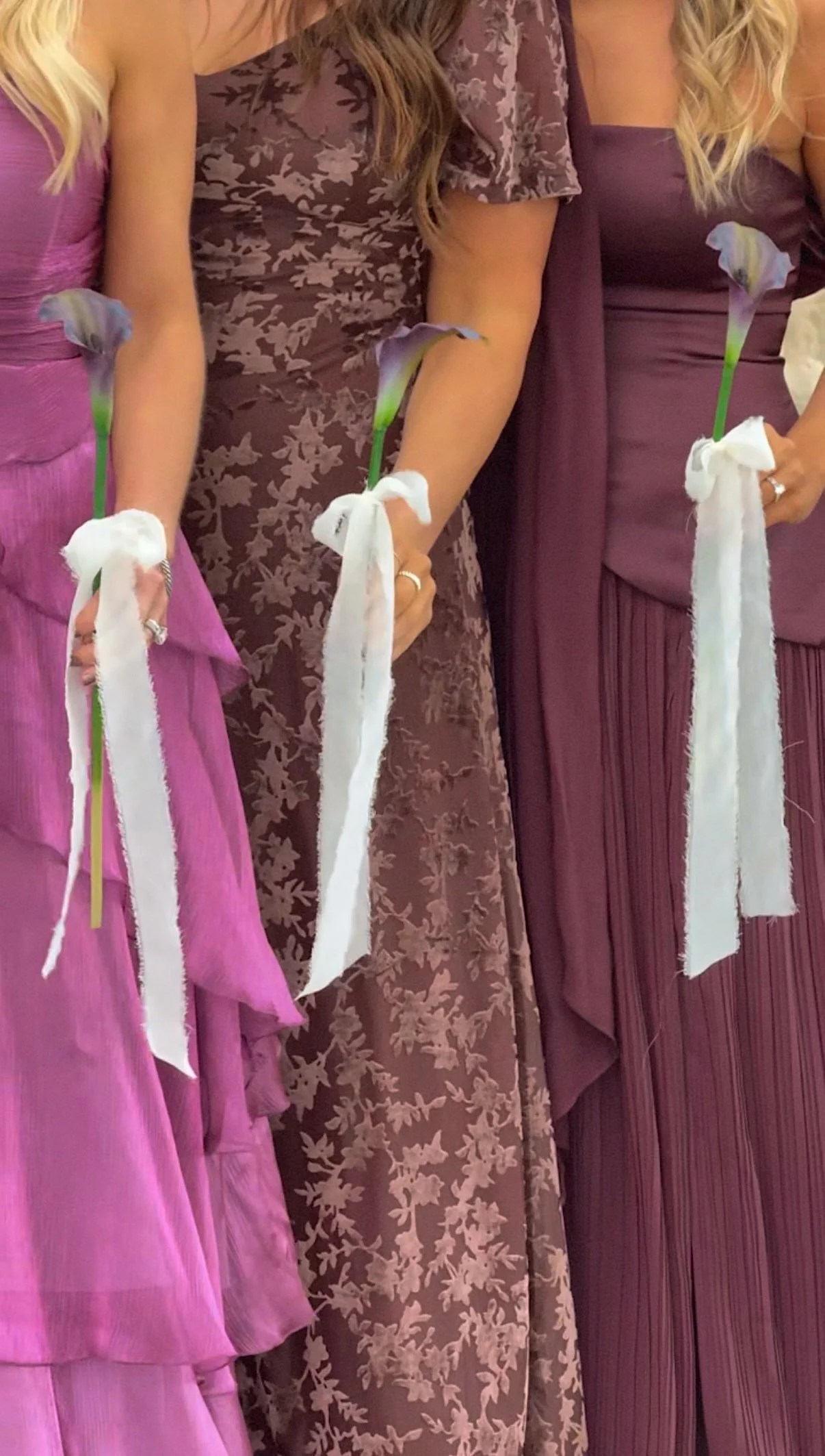 People in elegant dresses holding calla lilies with white ribbons at a celebration or event.