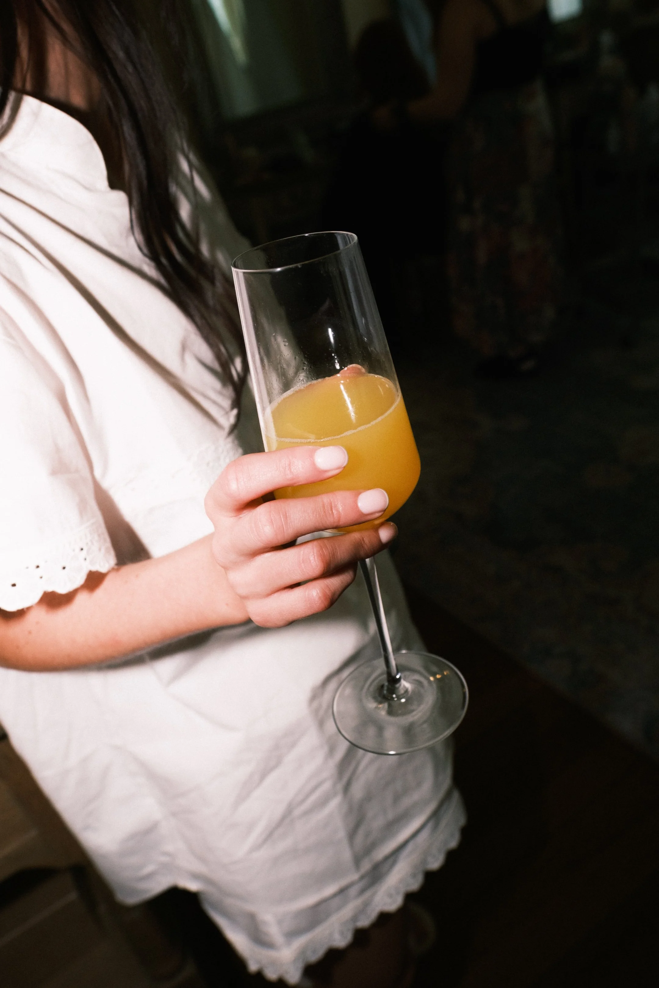 Woman holding a glass of orange juice in a dimly lit indoor setting.