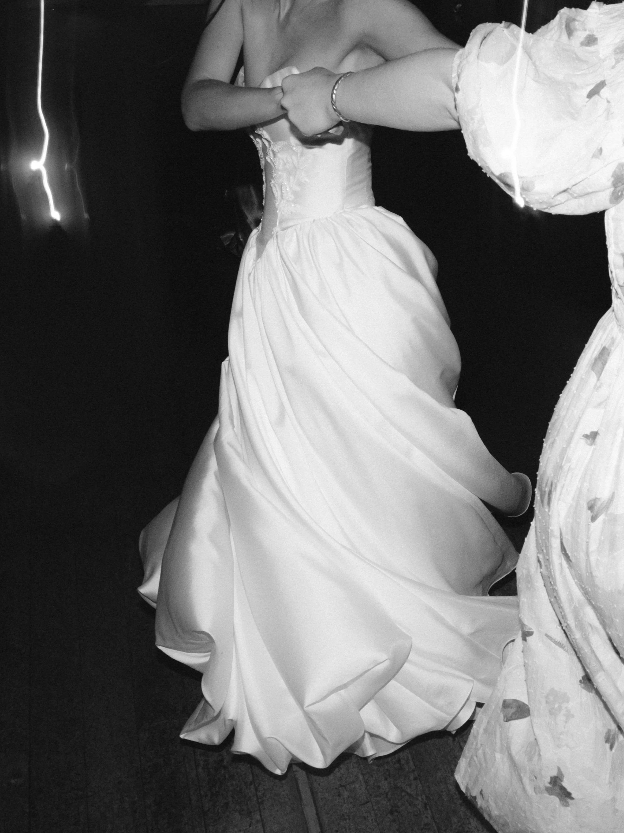 A person in a wedding dress holding hands with another person during a wedding dance, with a dark background.