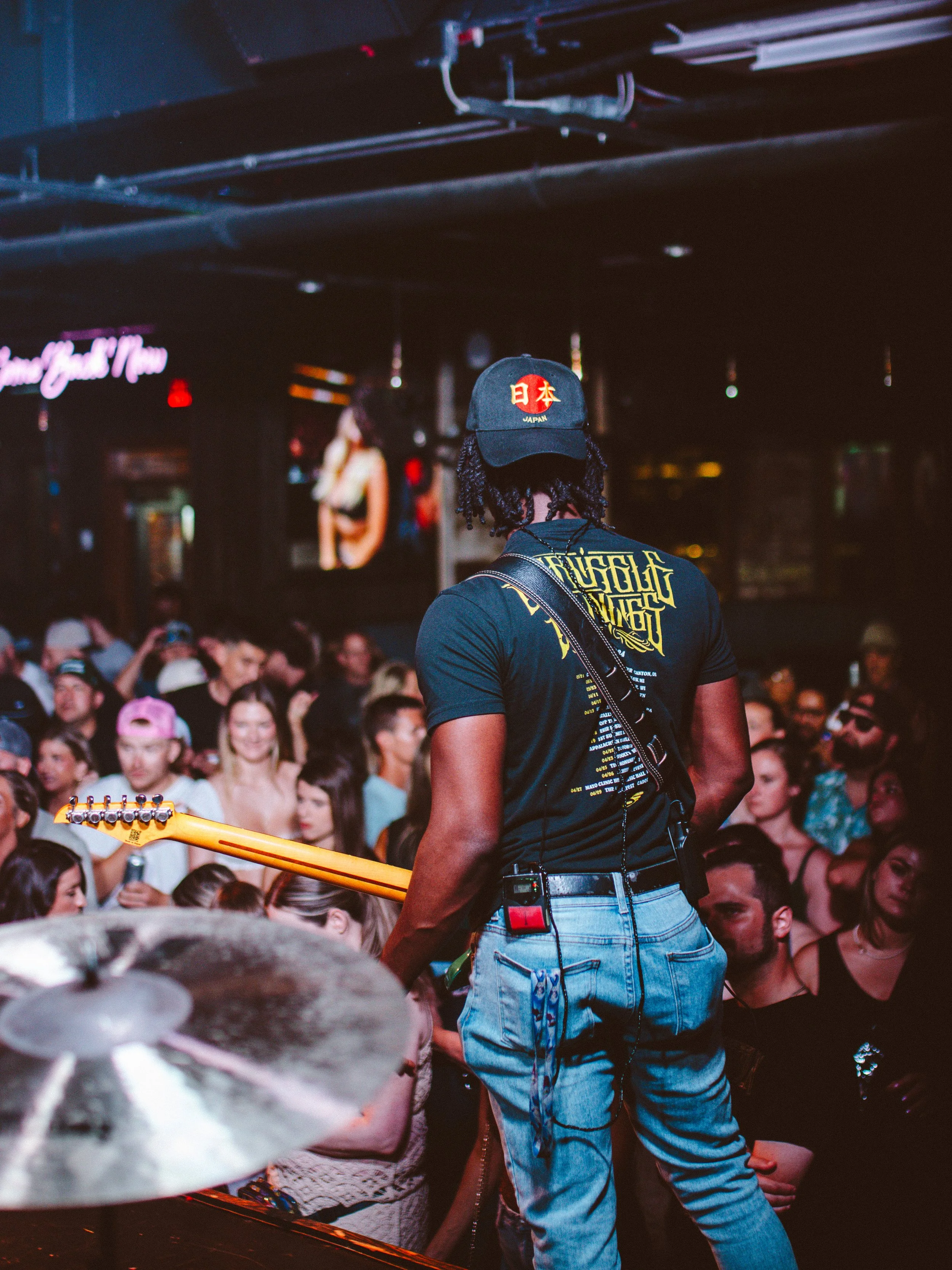 Musician performing on stage with a guitar at a crowded indoor concert venue.