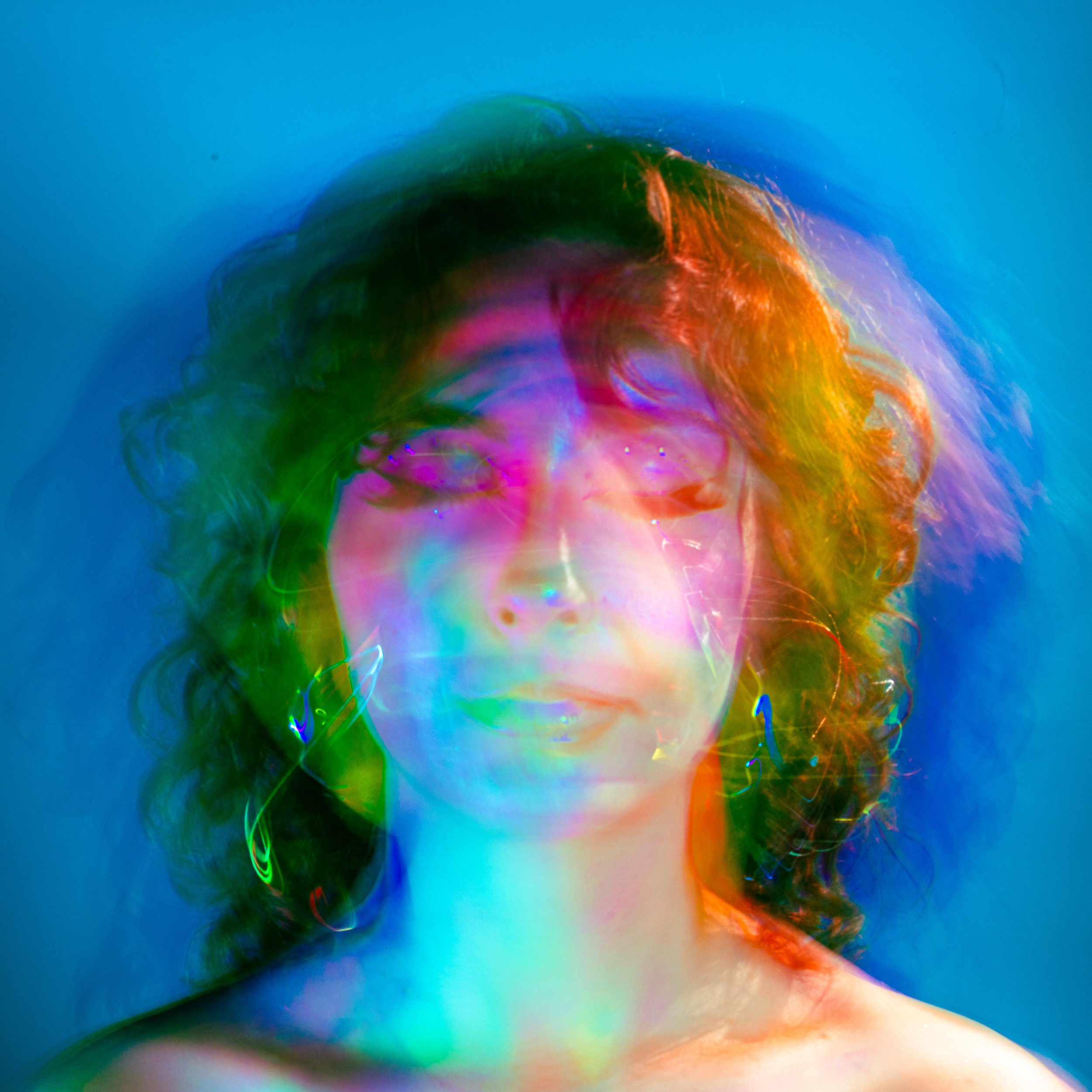 A portrait of a woman with curly hair, illuminated by colorful, overlapping light trails creating an abstract, vibrant effect.