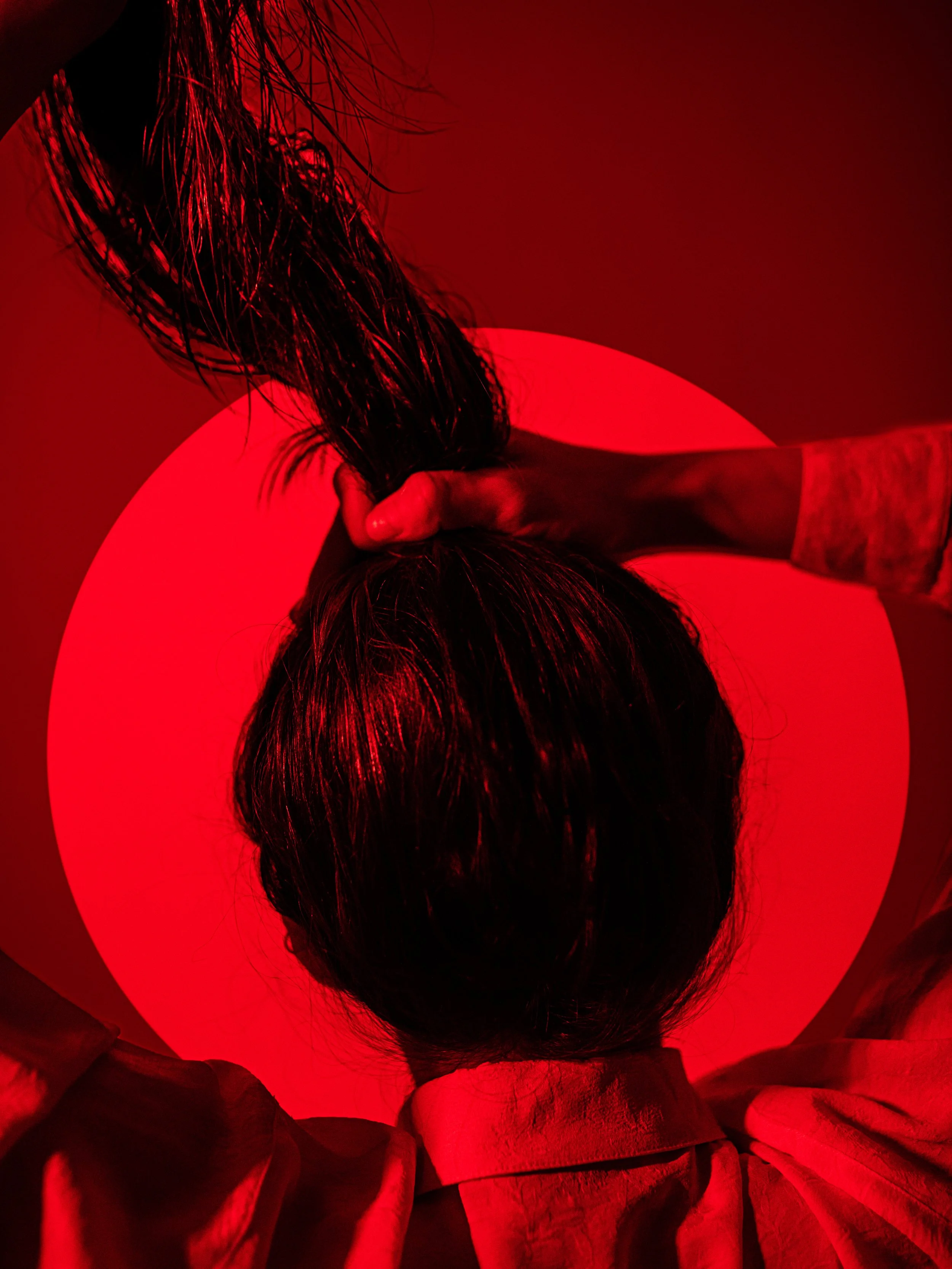 Person holding long, wet hair against a red circular light, viewed from above.