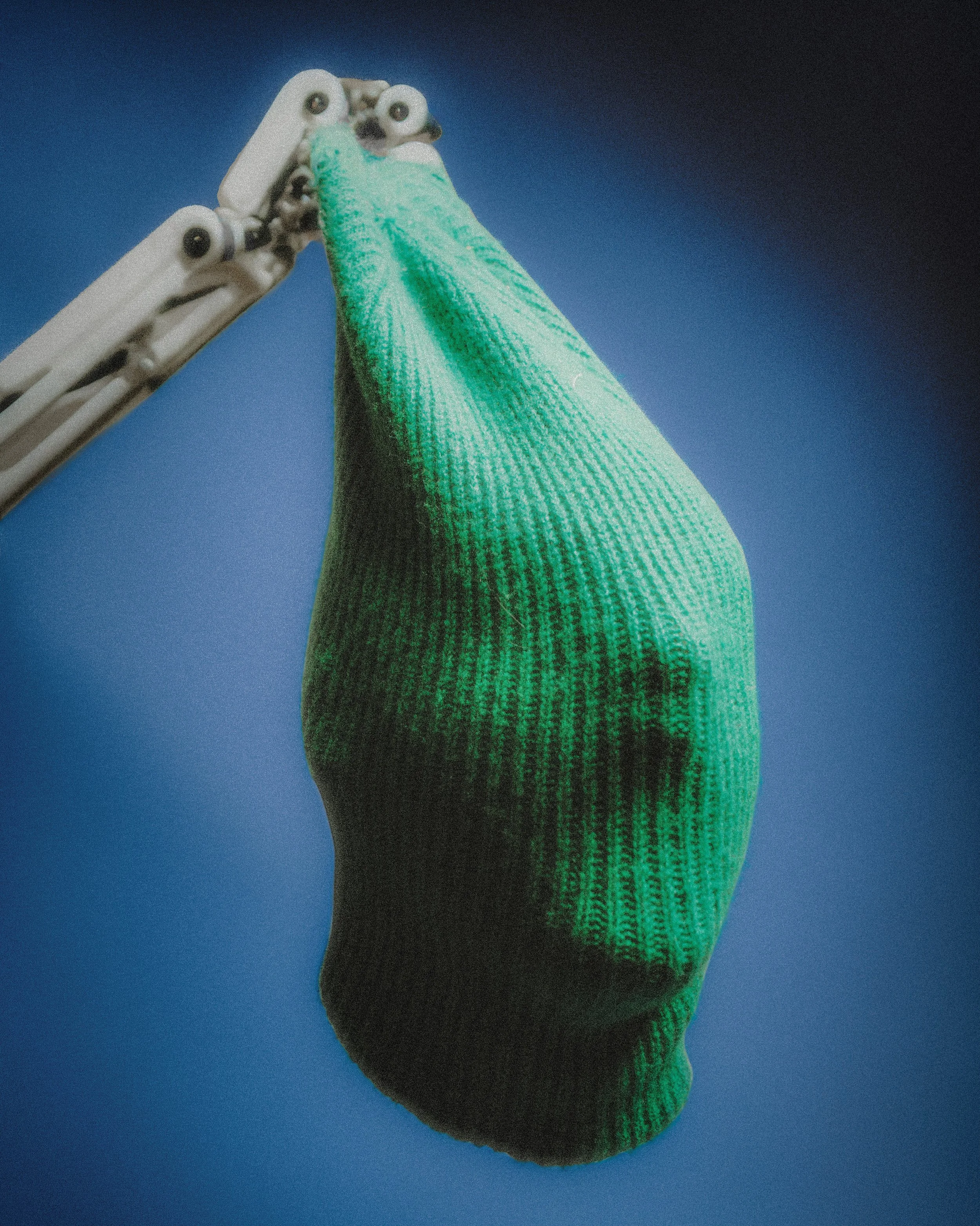 A robotic arm holding a green sock against a blue background.
