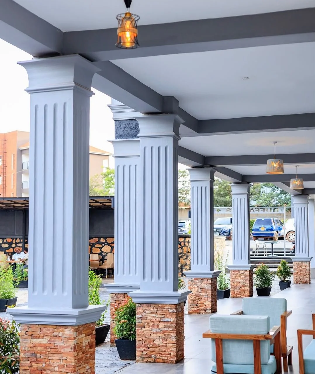 Outdoor covered patio with white columns and brick bases, hanging lights, potted plants, and seating area.