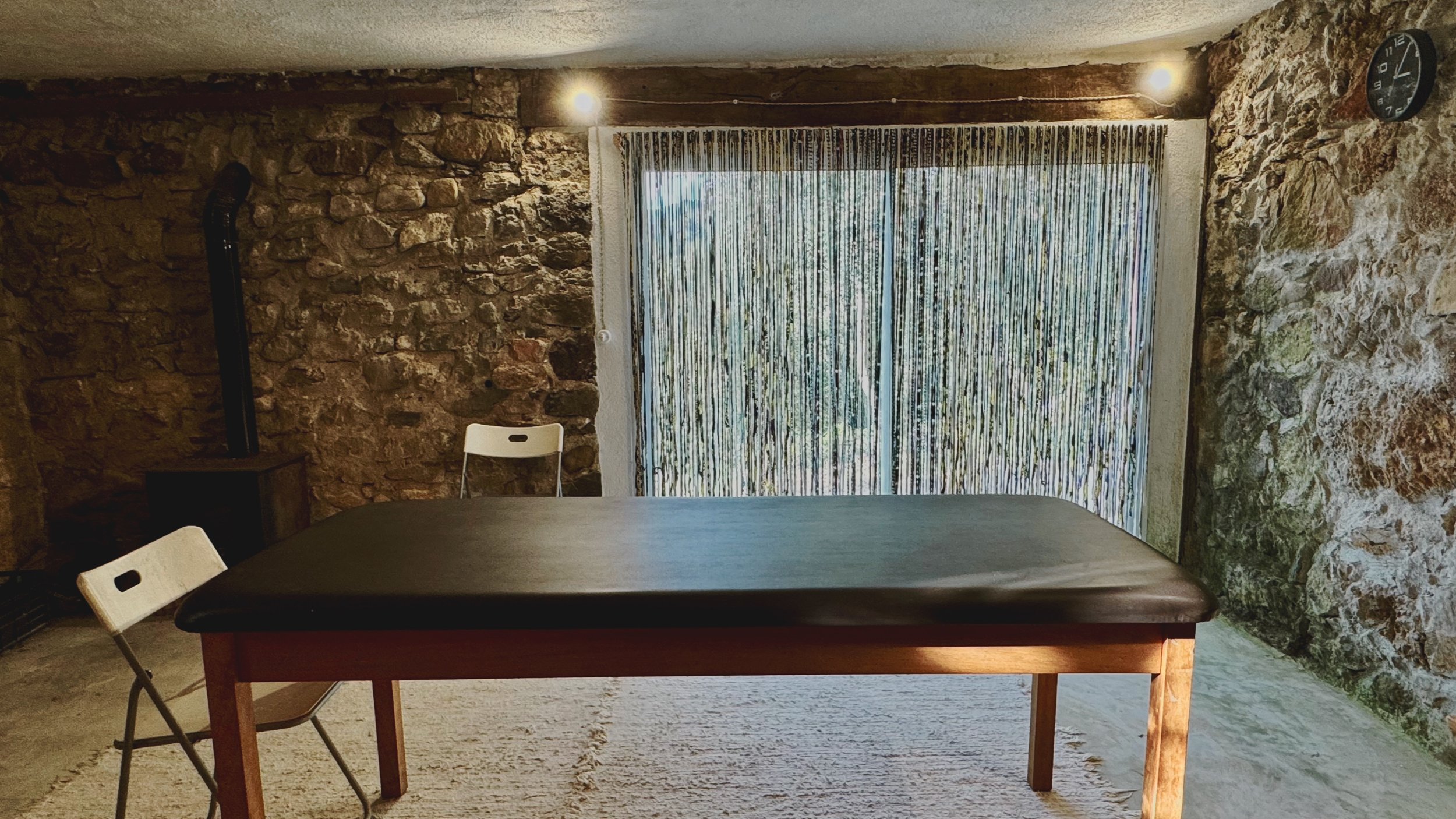 rustic stone room with a massage table and chairs for bodywork