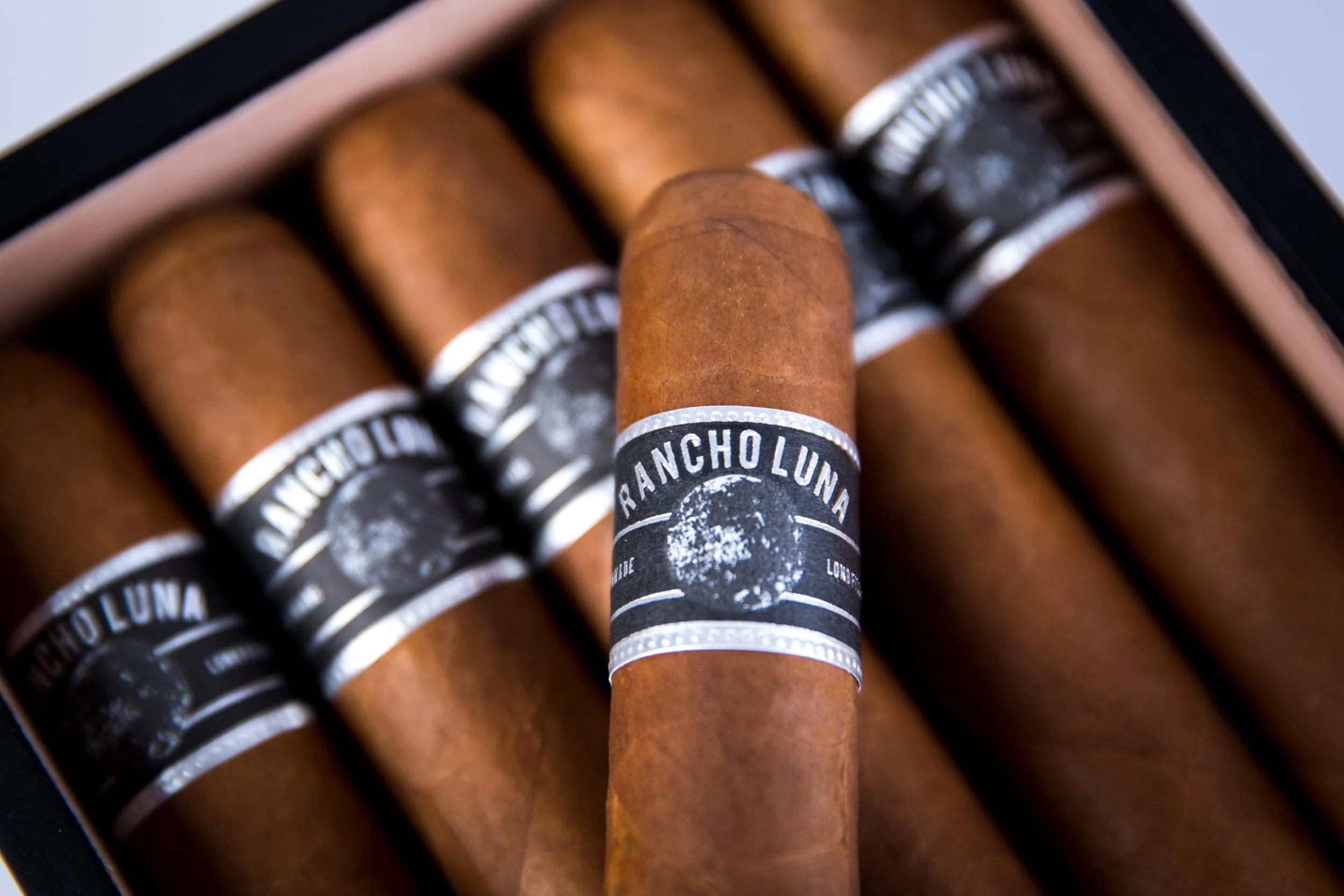 A box of cigars with one cigar in front, labeled 'Rancho Luna' and featuring a moon logo.