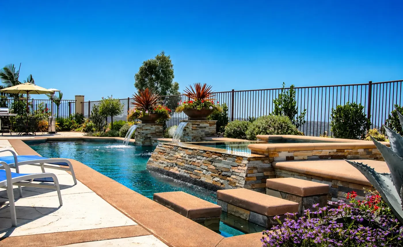 Luxury backyard with swimming pool, stone waterfall feature, potted plants, umbrella-shaded seating area, and a city view in the background.