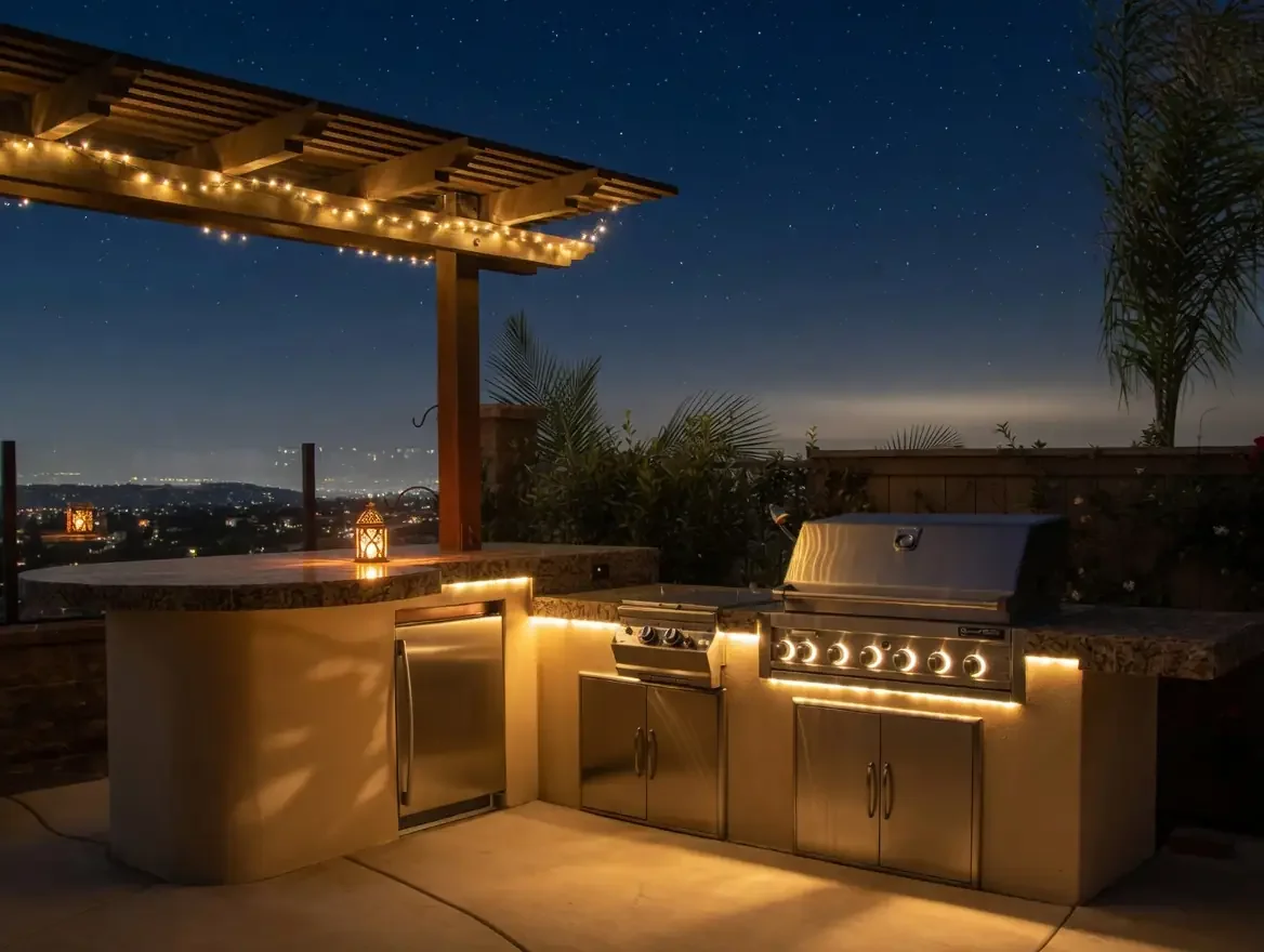 Outdoor kitchen with stainless steel grill, surrounded by string lights, under a wooden pergola with starry night sky in the background.