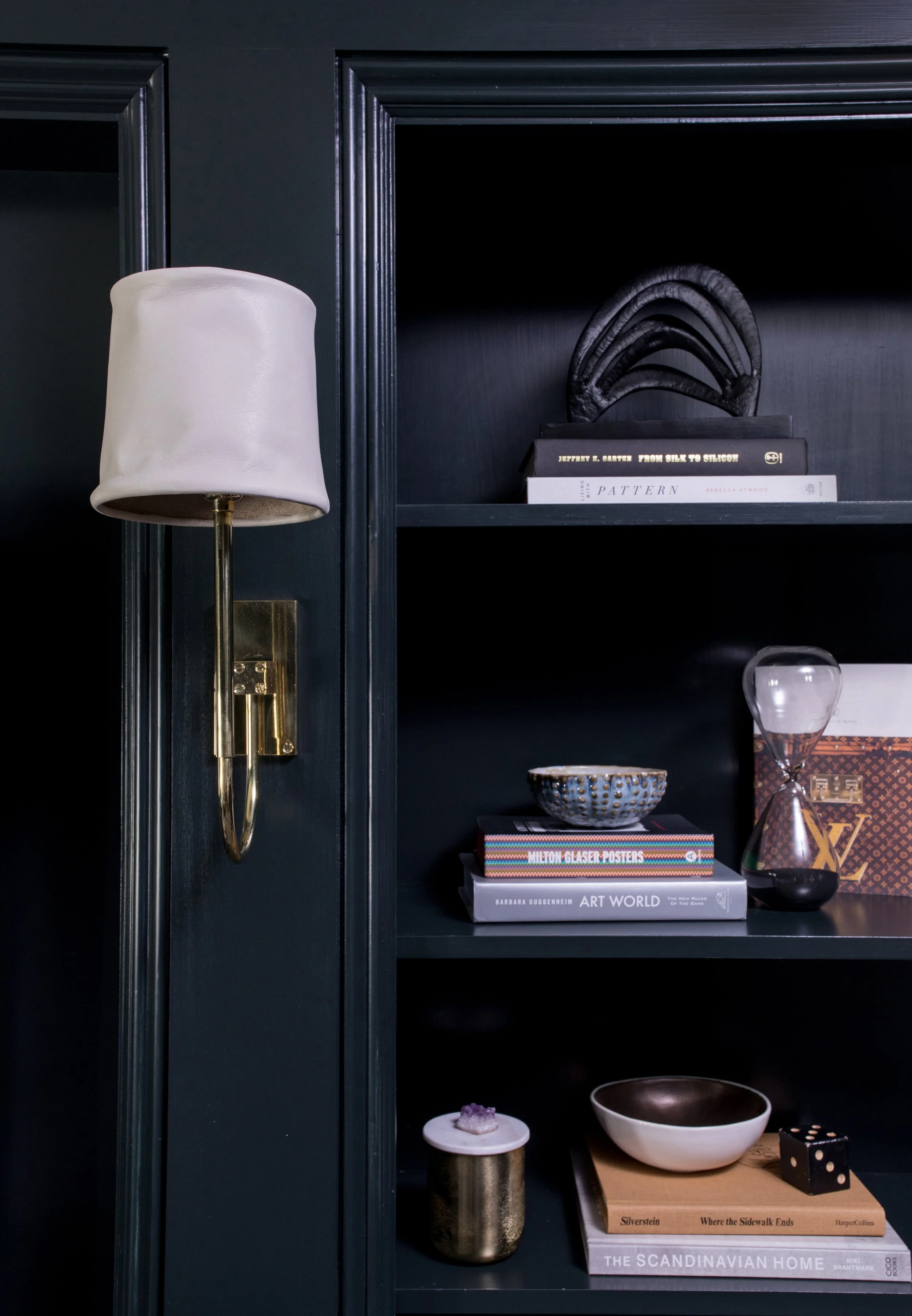 Dark blue bookshelf with decorative objects, books, a gold wall sconce, and a white speech lamp.