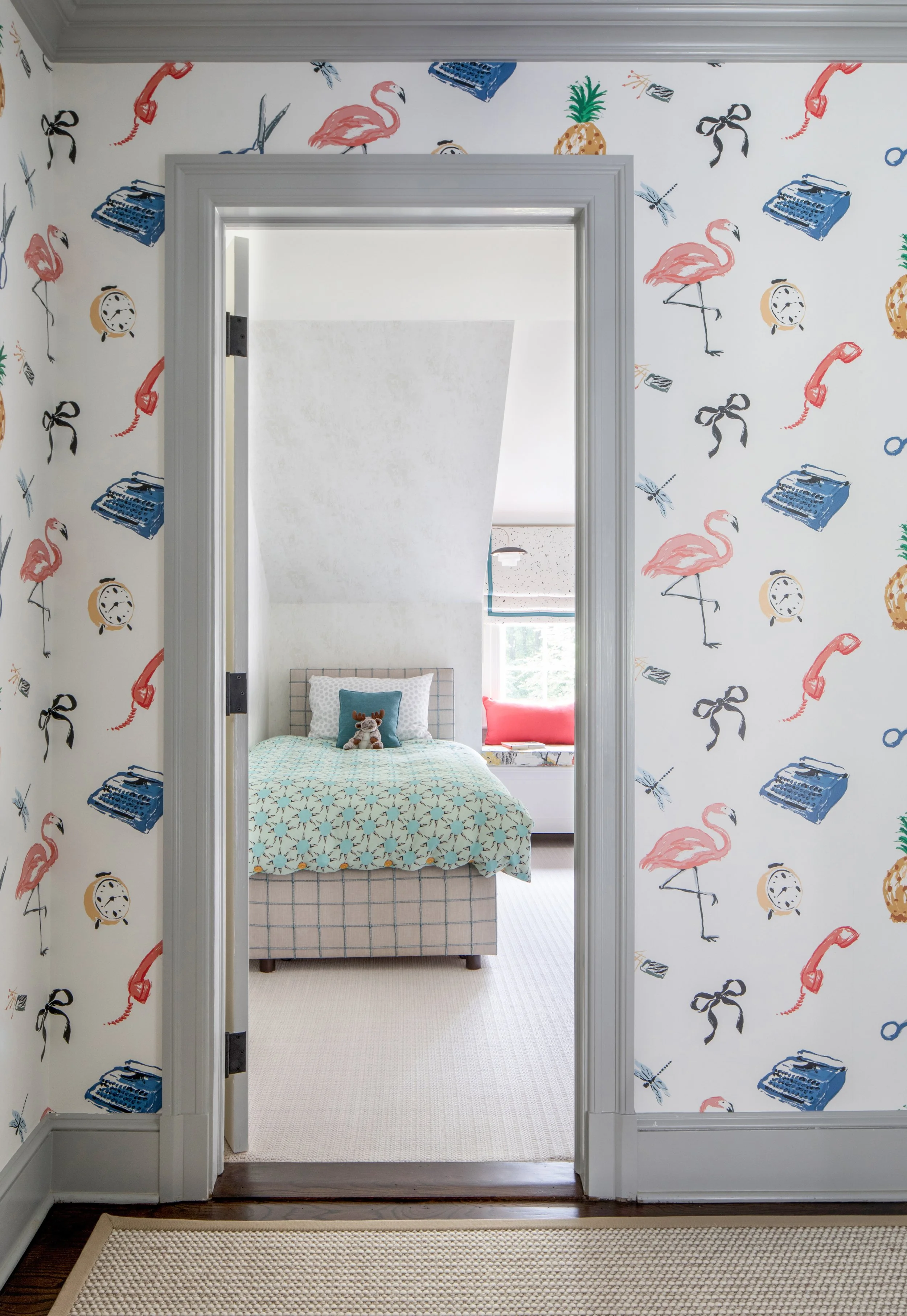 View of a bedroom through a door frame decorated with flamingo, pineapple, phone, clock, and book wallpaper.