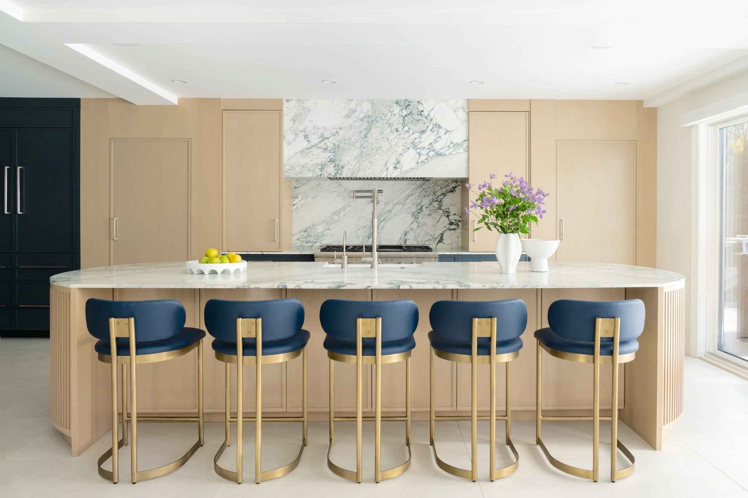 Modern kitchen with a marble island, blue and gold bar stools, and a marble backsplash.