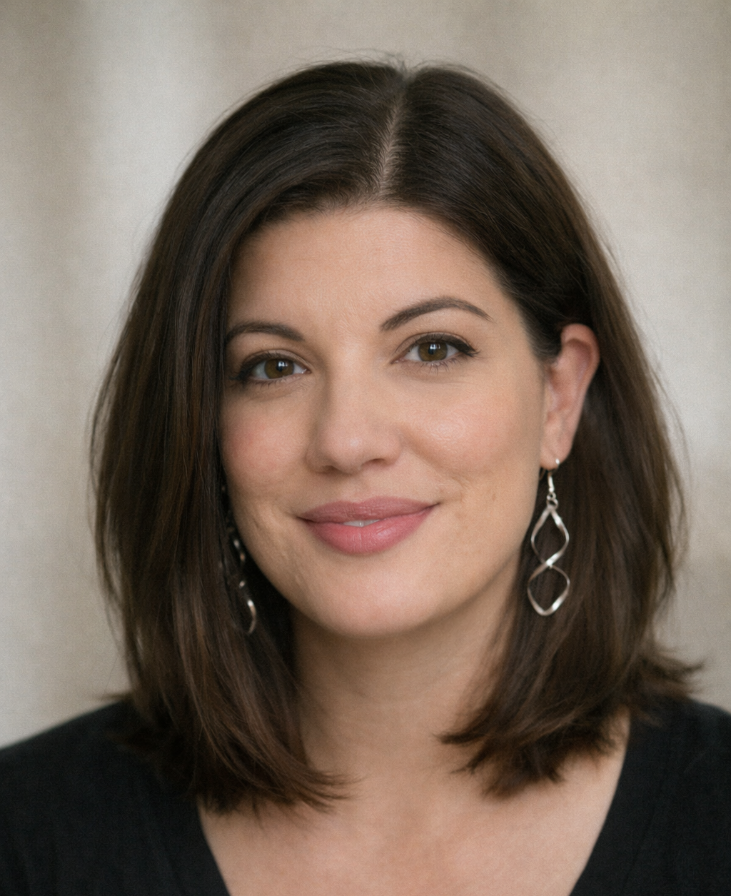 Portrait of a woman with shoulder-length brown hair, wearing earrings and a black top, smiling softly against a neutral background.