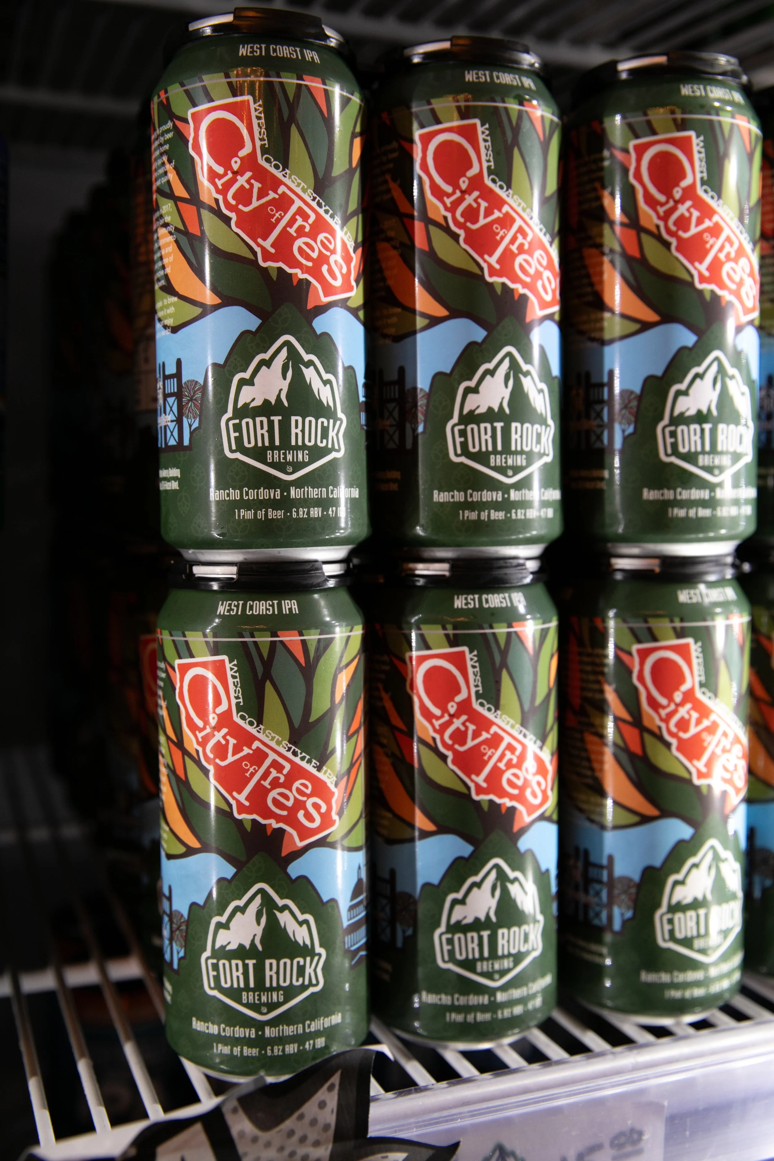 Cans of craft beer labeled 'City of Trees' from Fort Rock Brewing, West Coast IPA, on store shelves.