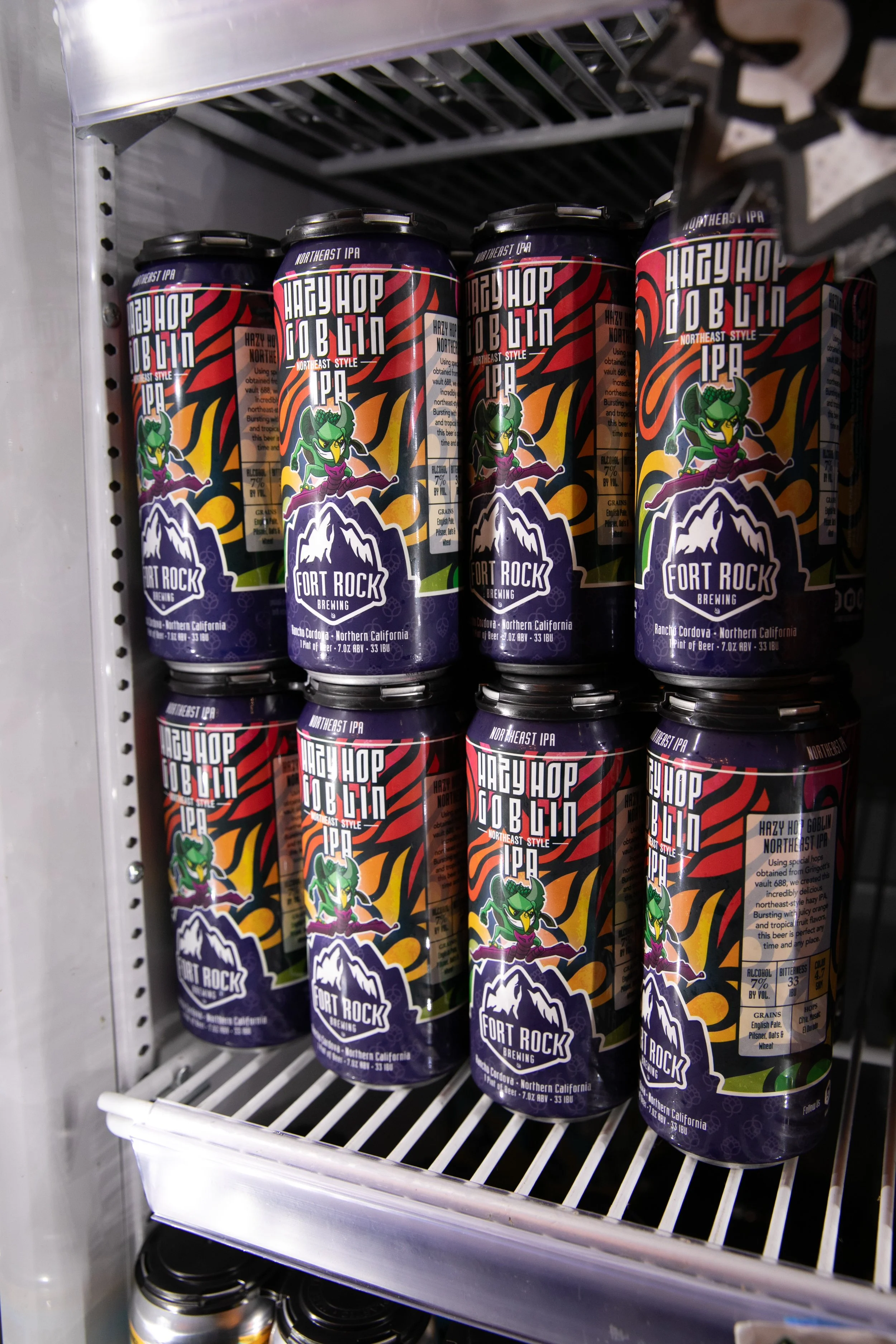 Cans of hazy hot goblin NE style IPA beer with cartoon goblin on label, on store shelf.