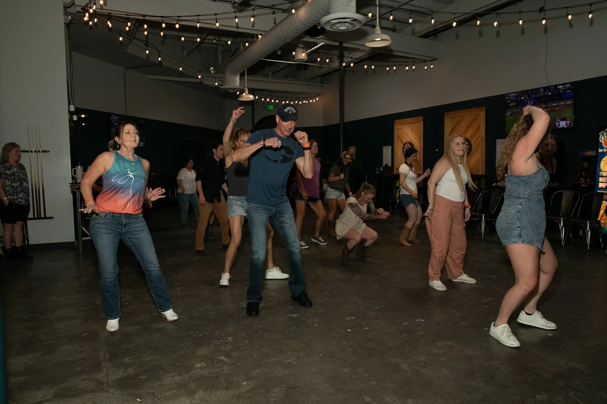 Group of people dancing and having fun in a dimly lit indoor space with string lights overhead.