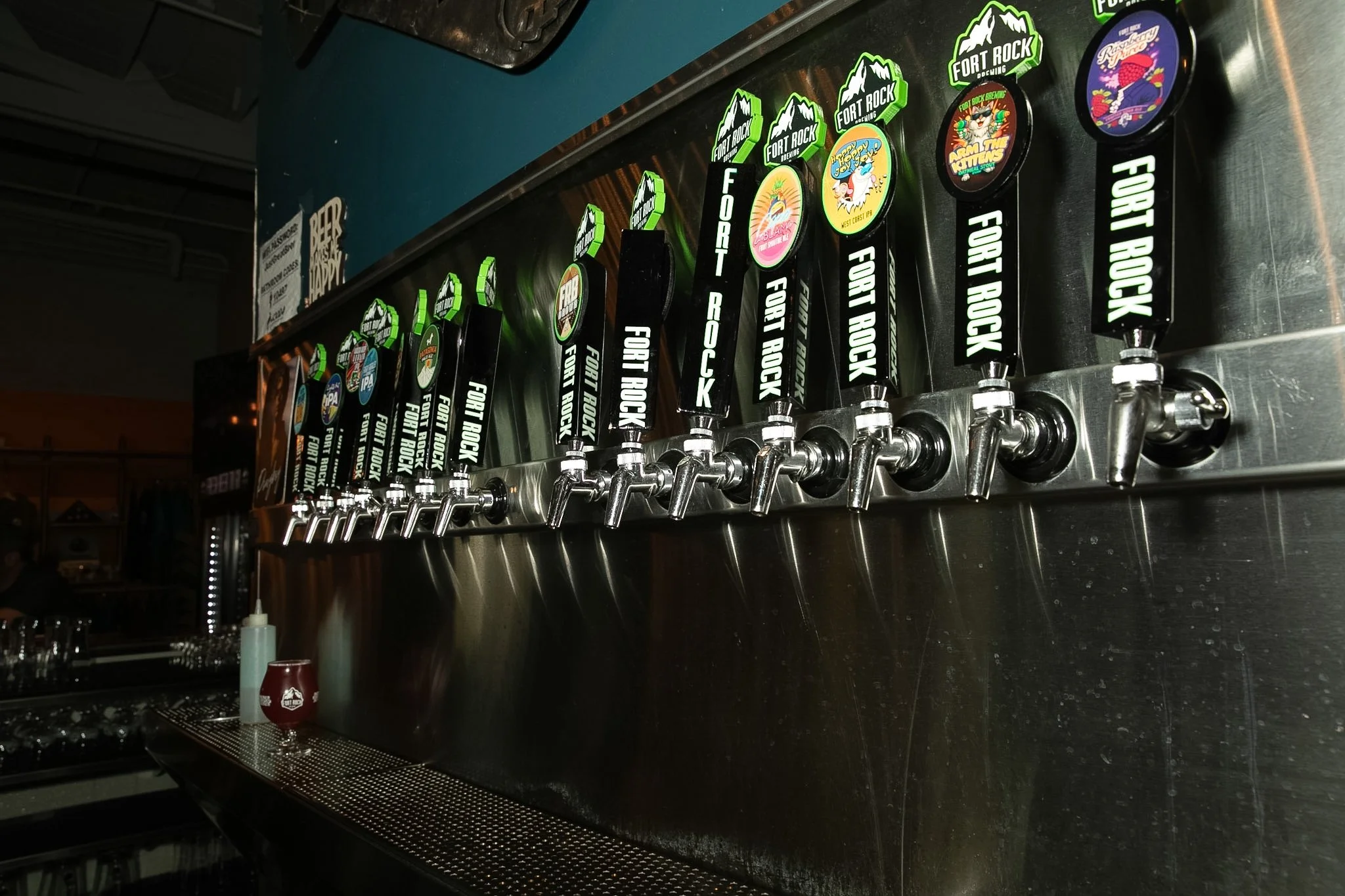 Tap handles on a beer draft system featuring various craft beer brands, including Fort Rock Brewing and others, on a dark countertop at a bar.