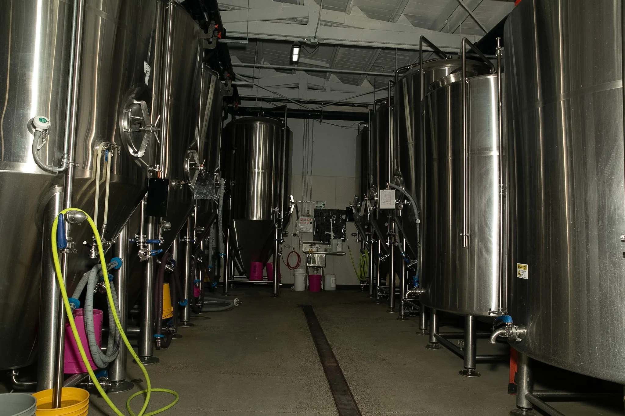 A row of large stainless steel fermentation tanks in a brewery or industrial brewing facility.