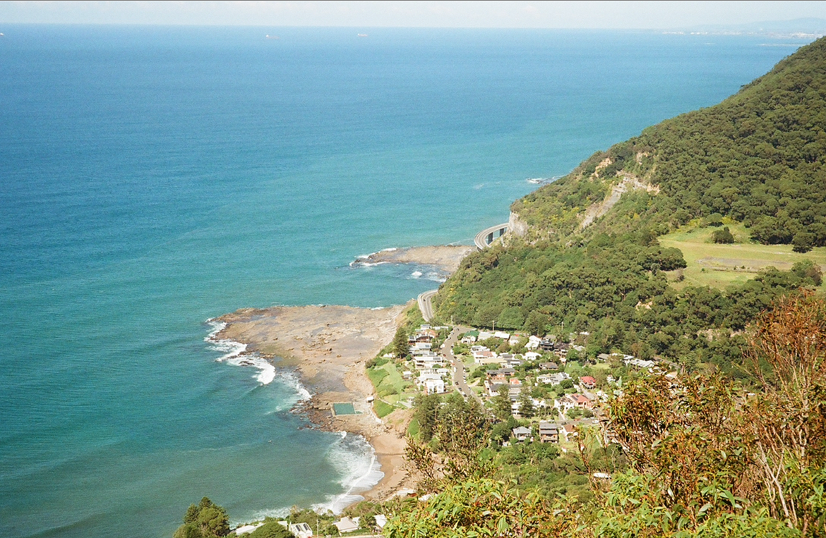 Aerial view of a small coastal town nestled along the shoreline and surrounded by lush green hills.