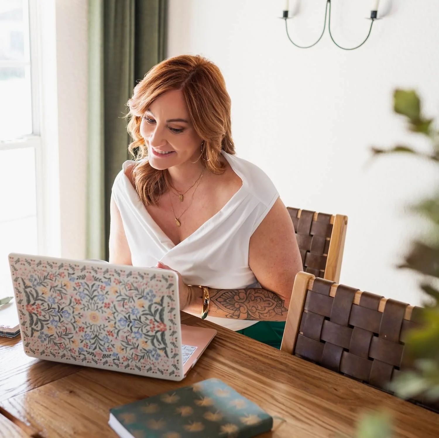 Dietitian sitting at a kitchen table working on a laptop, focused and smiling while provided nutrition counselling online