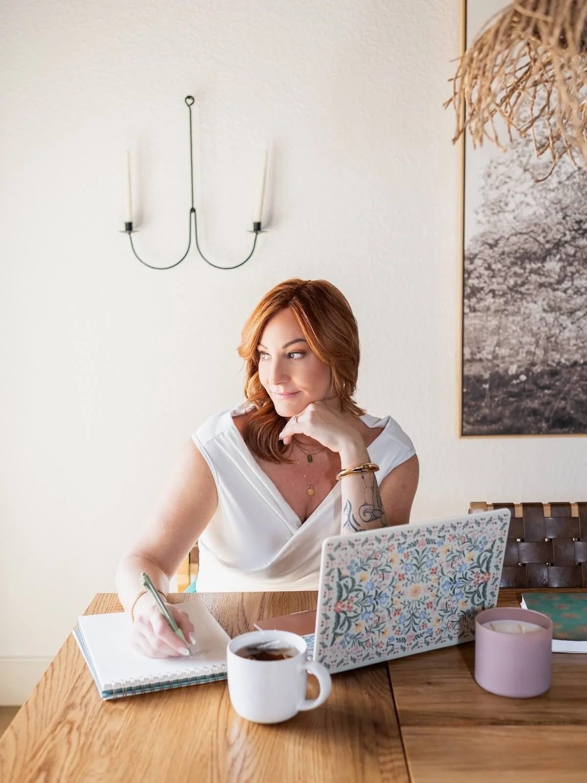 Torree sitting at a table with her laptop, notebook, candle and a cup of tea.