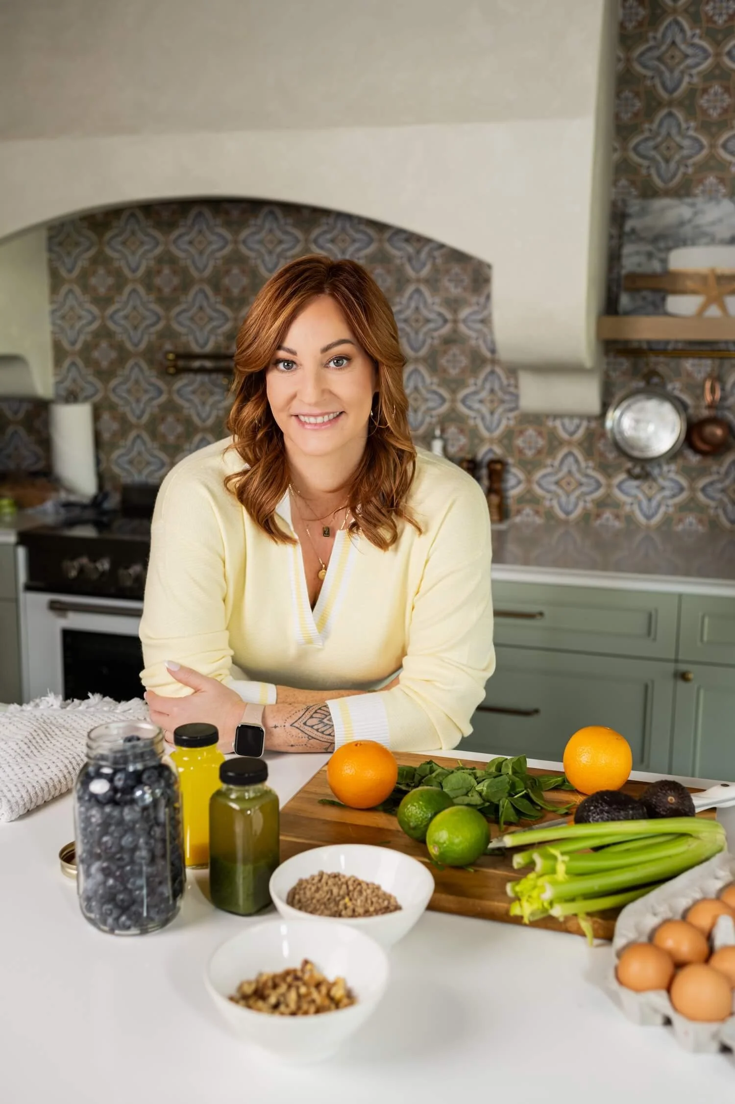 Torree leaning at a kitchen bench with fresh ingredients and prepared dishes in front of her.