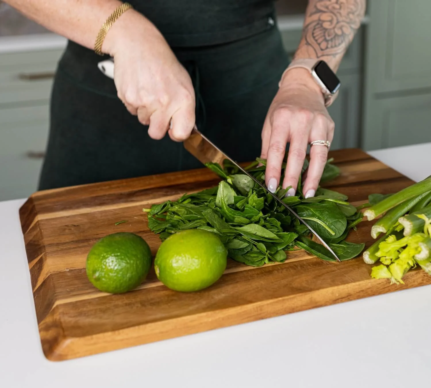 Hands slicing spinach and limes on a wooden cutting board.