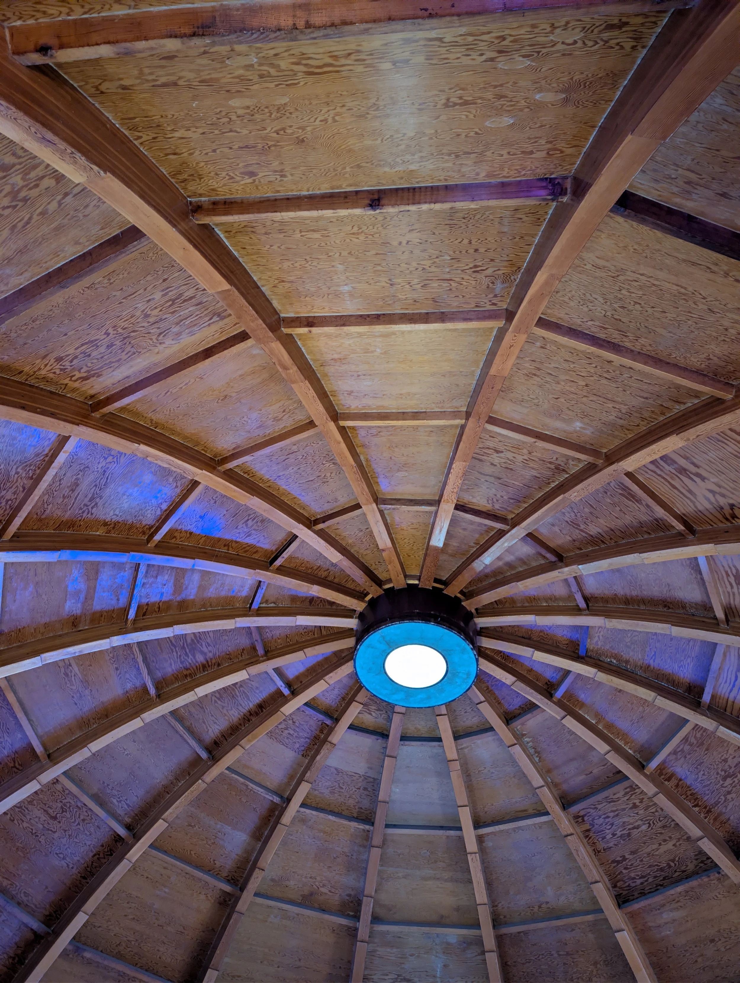 View of a wooden ceiling with a central circular light fixture emitting blue and white light.