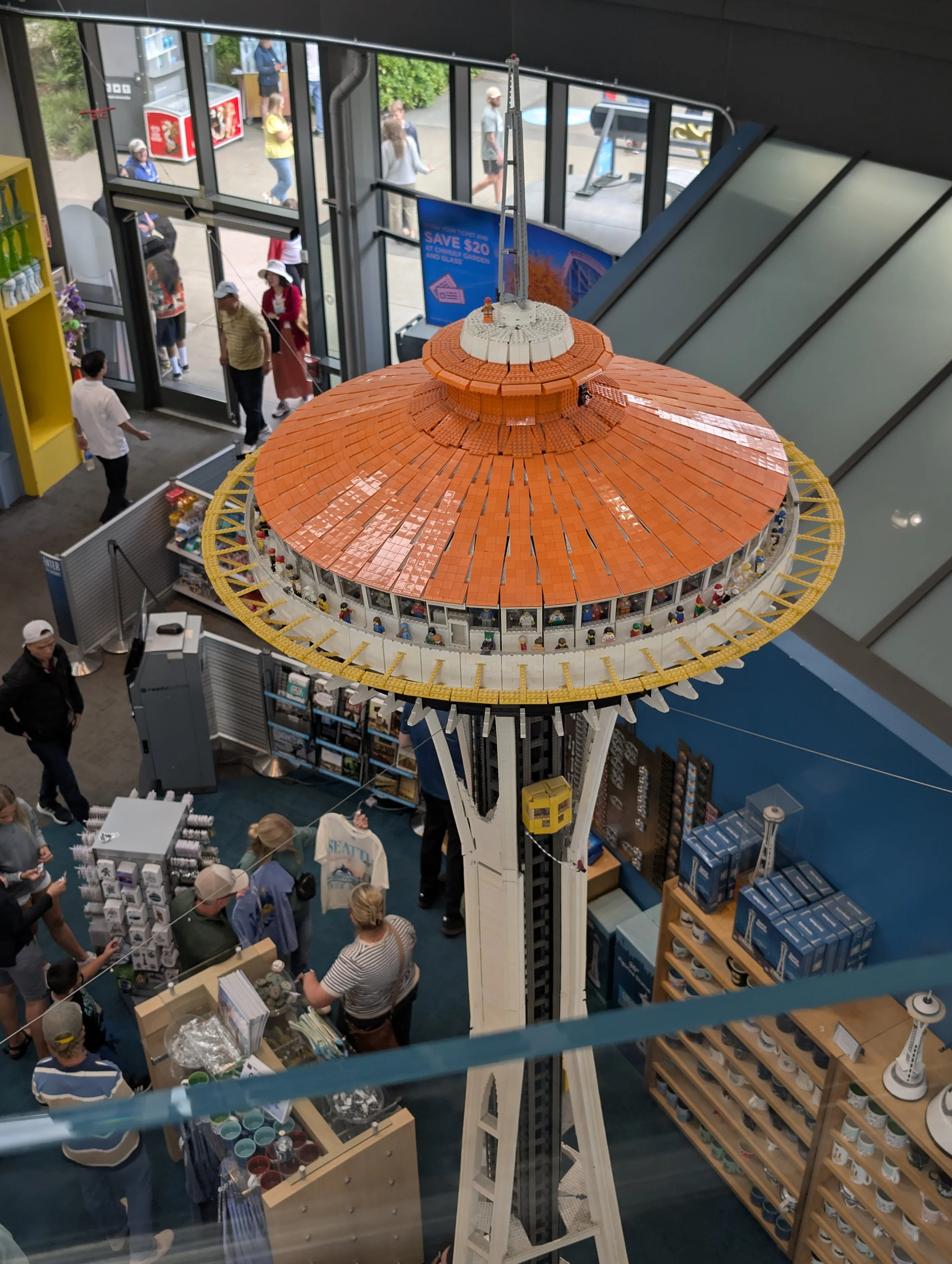 Interior view of a store with a LEGO replica of the Space Needle, with several people shopping and conversing around the display.