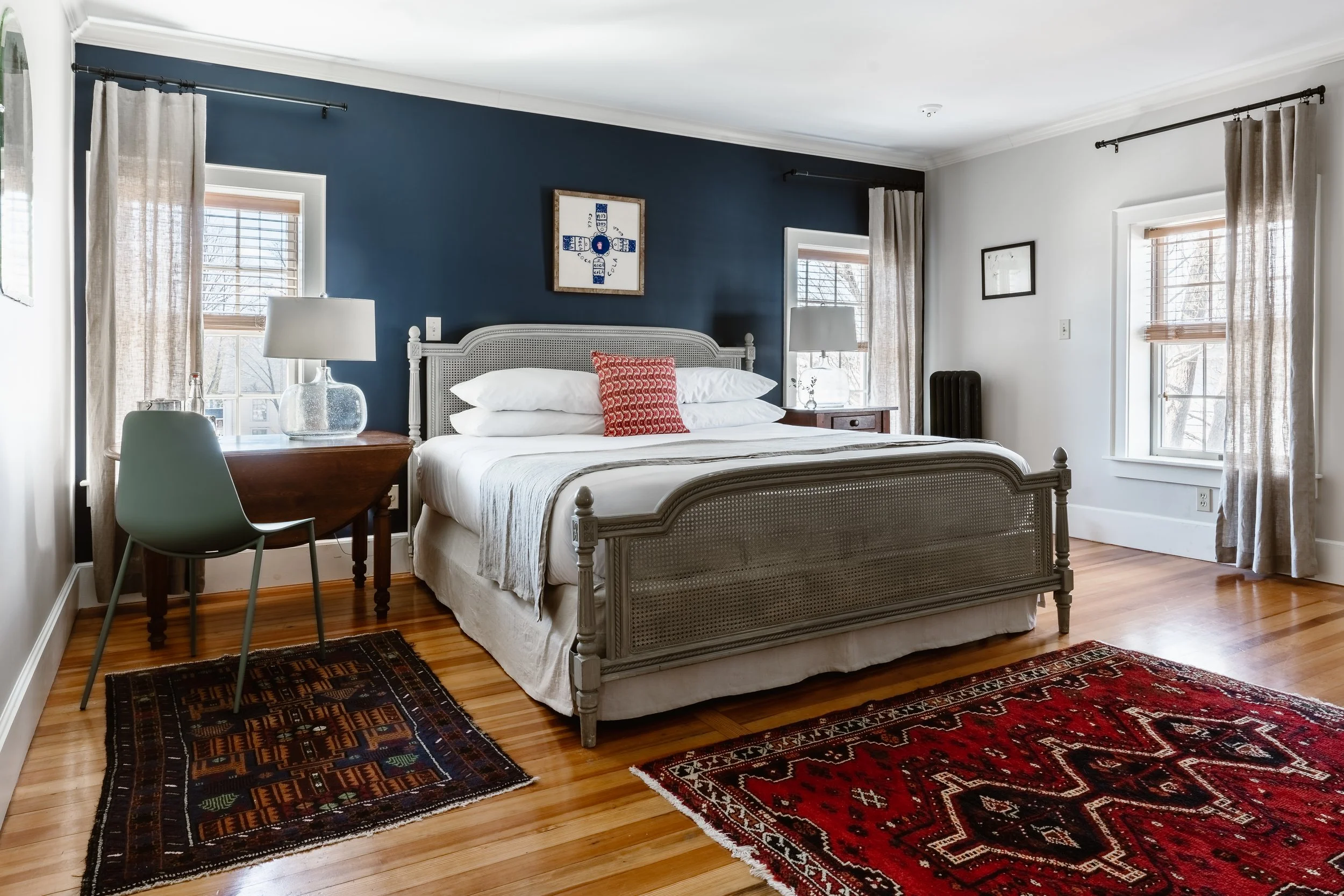 Airy hotel room with bed, desk, wood floors and rugs