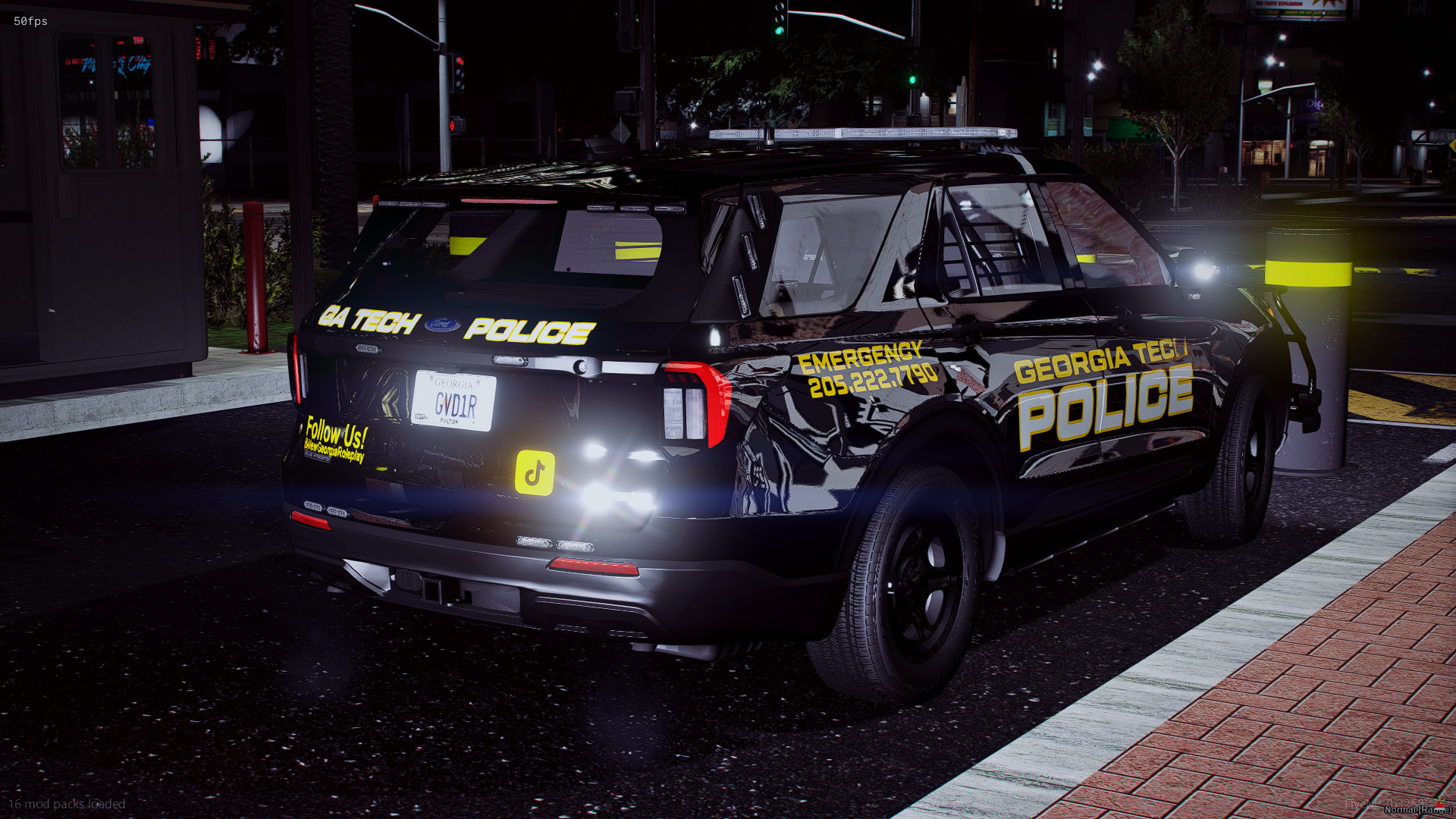 A black Georgia Tech police SUV parked at night on a city street. The vehicle has emergency lights on, with yellow and white text on the sides indicating police and emergency contact information. The street has brick and concrete sidewalks, and in th