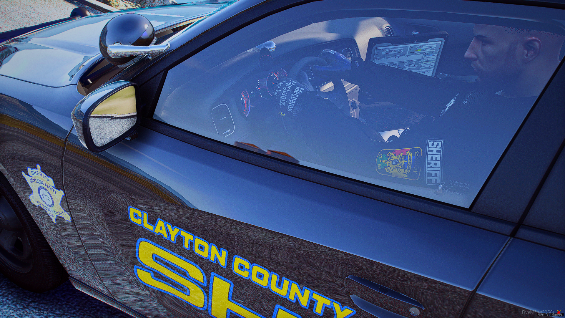 A police car with Clayton County sheriff's badges on the door, viewed from the side, parked on a gravel surface.