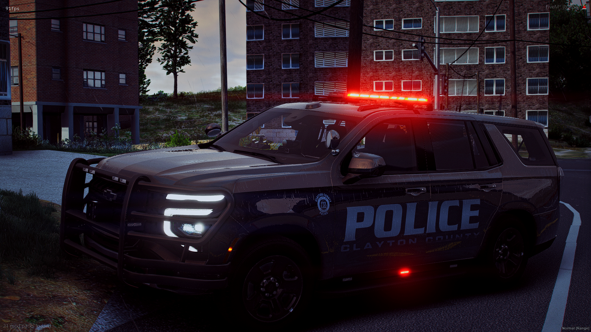 A Clayton County police vehicle with flashing red lights parked on a residential street at dusk, with multi-story apartment buildings in the background.