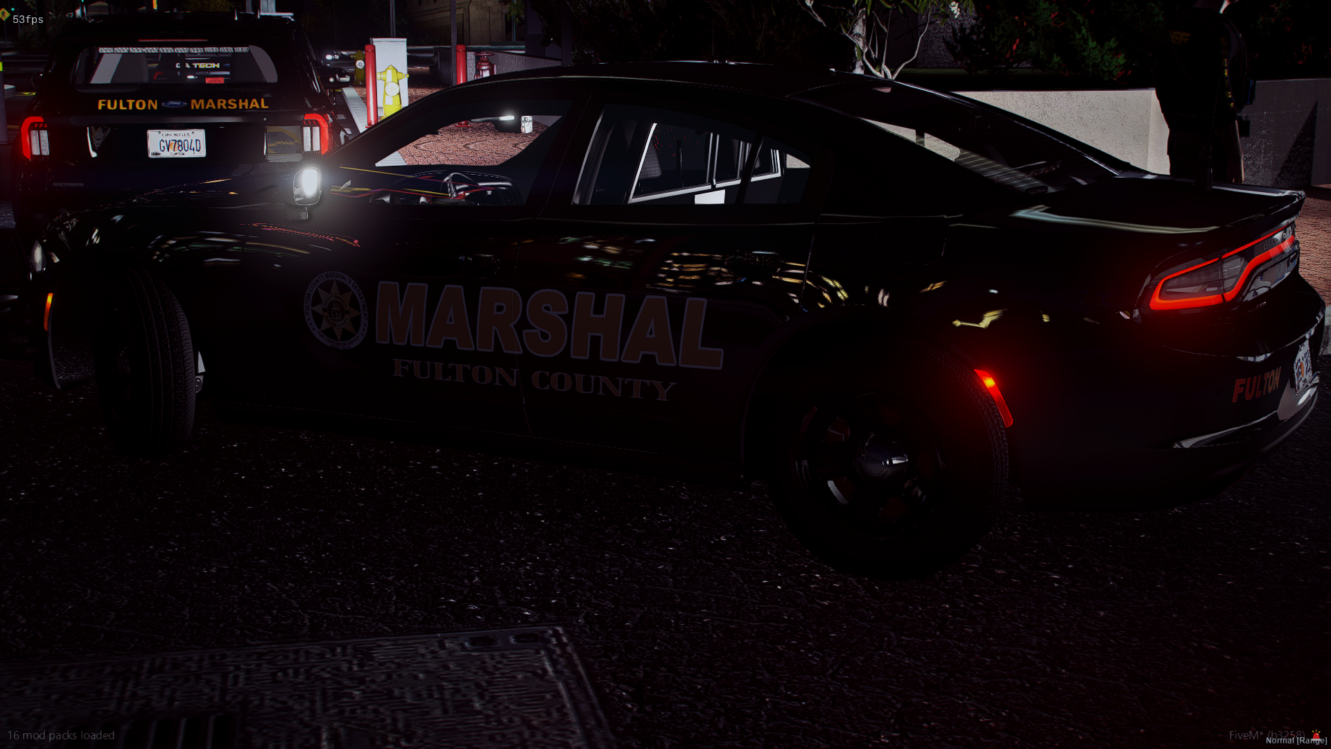 A black police car with marked 'Marshal' from Fulton County is parked at night, with other vehicles and police officers nearby.