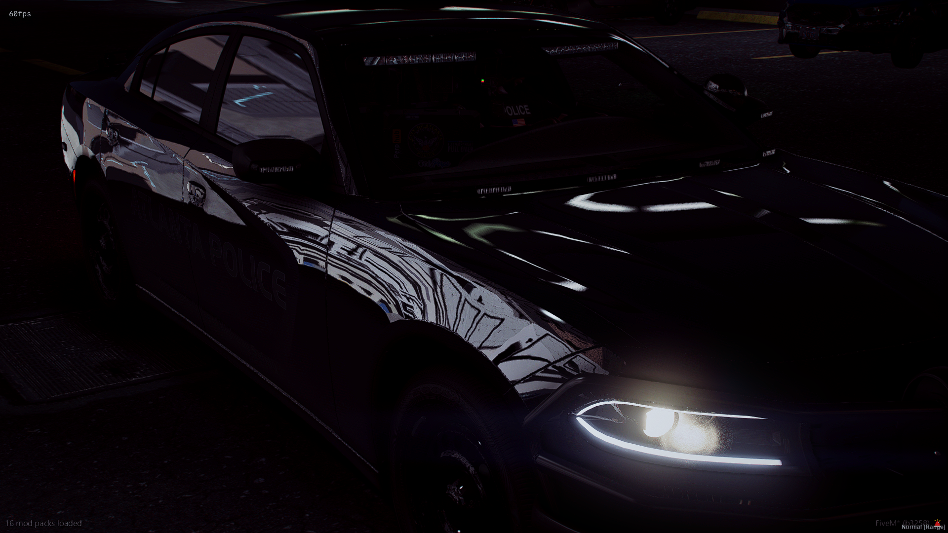 A black police car parked in a dark parking lot, with one of its headlights on and reflections from the surrounding area visible on its surface.