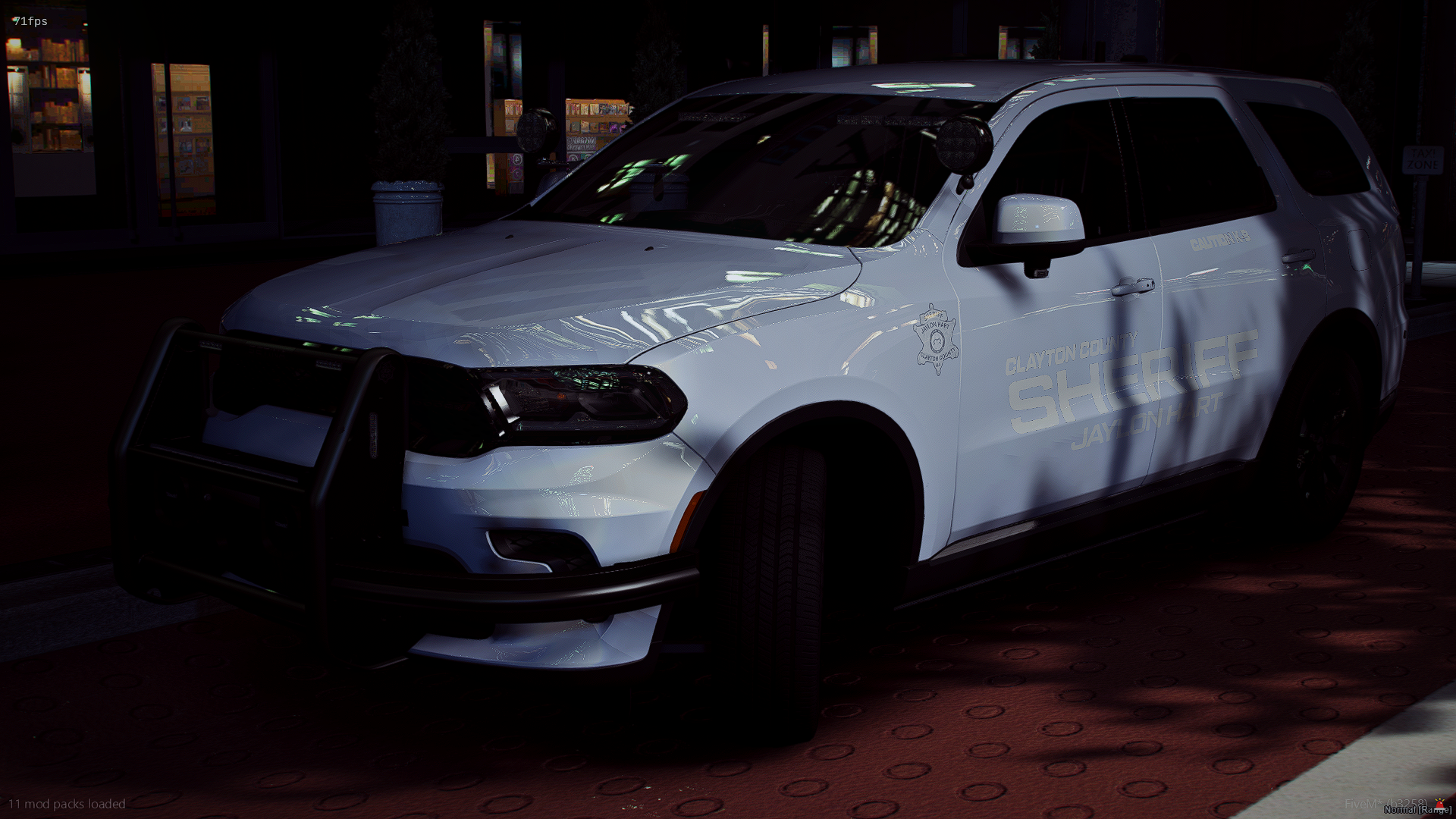 A white Clay County Sheriff vehicle parked in a dark area, possibly a parking lot, with reflections of overhead lights on its surface.