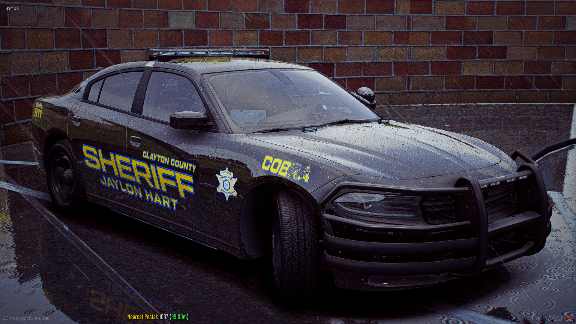 A black Clayton County Jaylon Hart sheriff police car with police markings and a light bar on top, parked against a brick wall with water on the ground.
