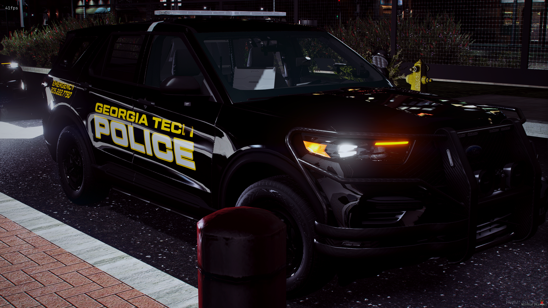 A black Georgia Tech police SUV parked on a street at night with its lights off. The vehicle has yellow and white markings, including the word 'POLICE' and 'EMERGENCY' along with a phone number. The street has a brick sidewalk, a red bollard, and a f