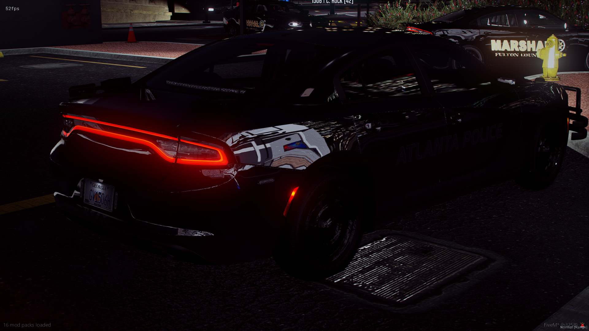 A black Atlanta police car with illuminated red taillights parked on a street at night. The vehicle has a Georgia license plate and is next to a yellow fire hydrant. There are other police vehicles and a fire hydrant in the background.