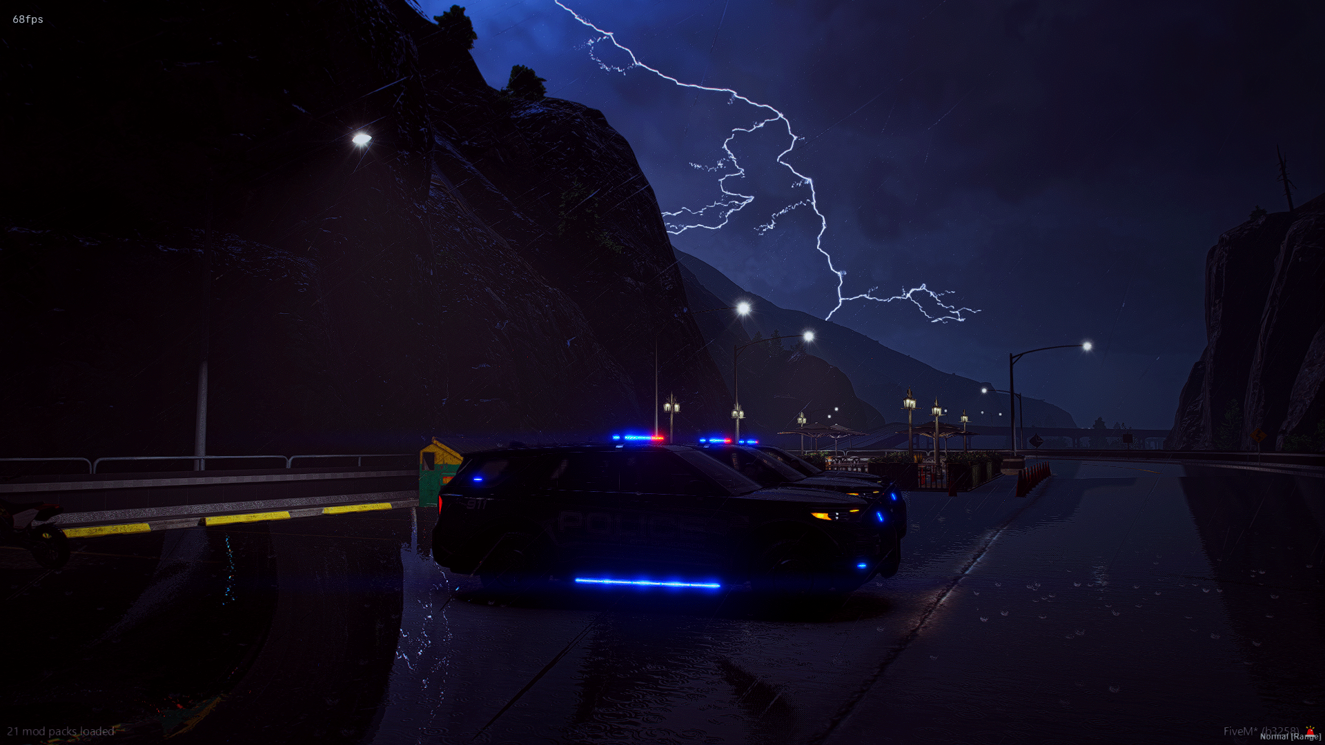 Night scene with lightning in the sky over a mountain landscape, a police car with flashing lights parked by the side of a wet road, street lamps, and a waterfront area with picnic tables.