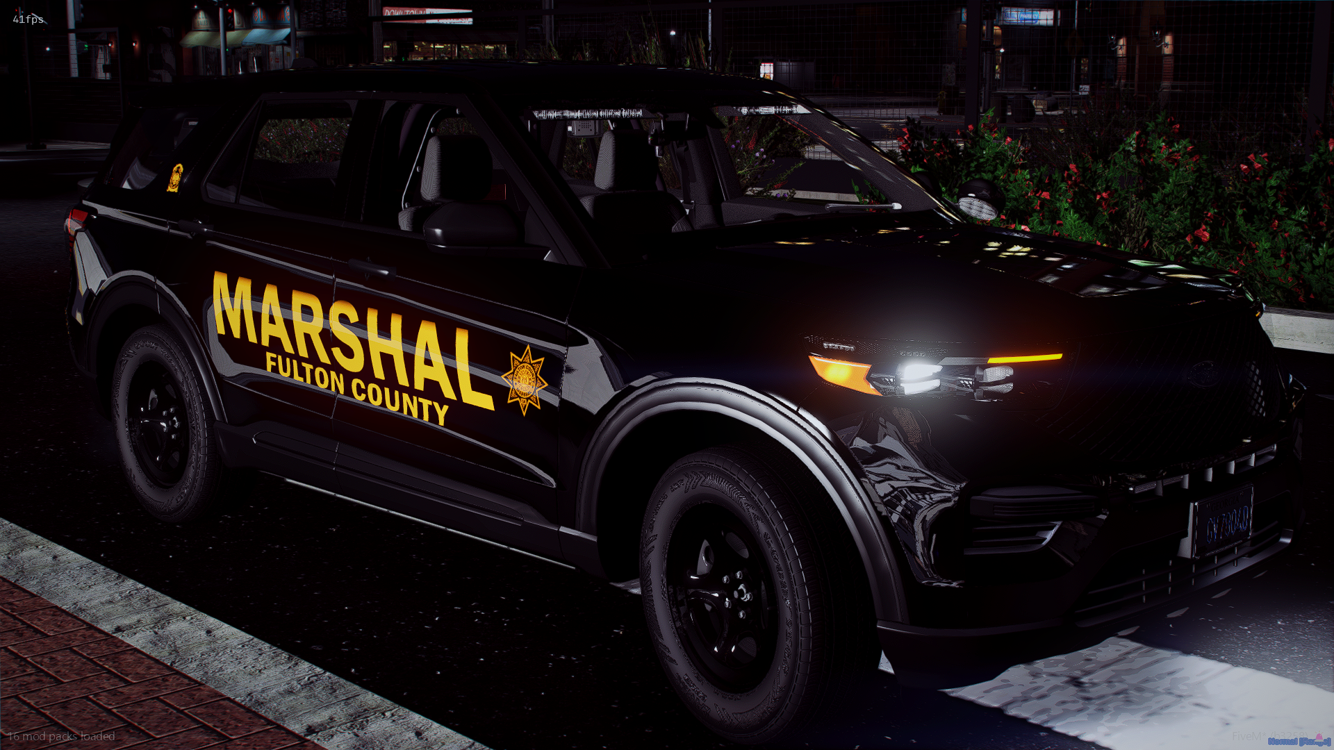 A black sheriff's patrol SUV from Fulton County with a yellow 'Marshal' decal, parked on a street at night, with surrounding bushes and buildings in the background.