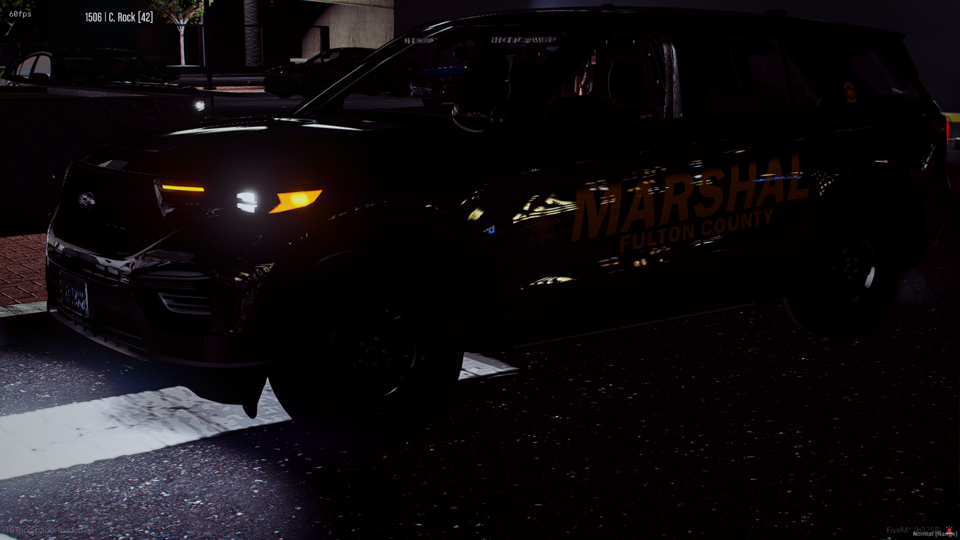 A dark police vehicle marked 'Marshall Fulton County' parked at night on a street, with other vehicles and buildings in the background. The police lights are not flashing.