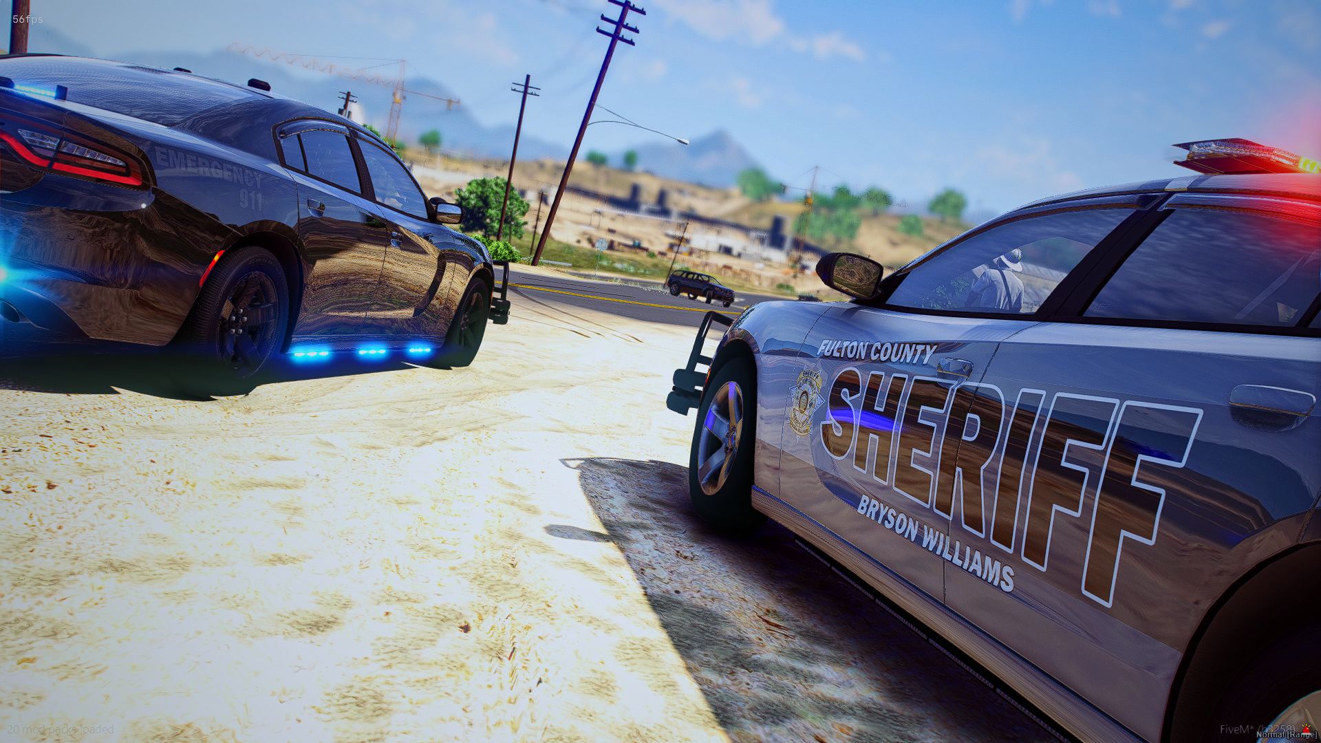 Two police cars are parked on a dirt area near a road, with one police car displaying flashing lights. The police cars are marked with 'Fulton County Sheriff's' and 'Emergency 911' insignias.